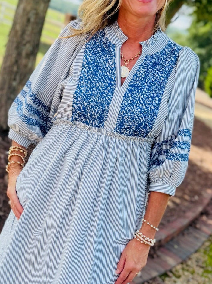Woman wearing Sherri Dress in blue striped midi length with embroidered bodice and three-quarter sleeves.