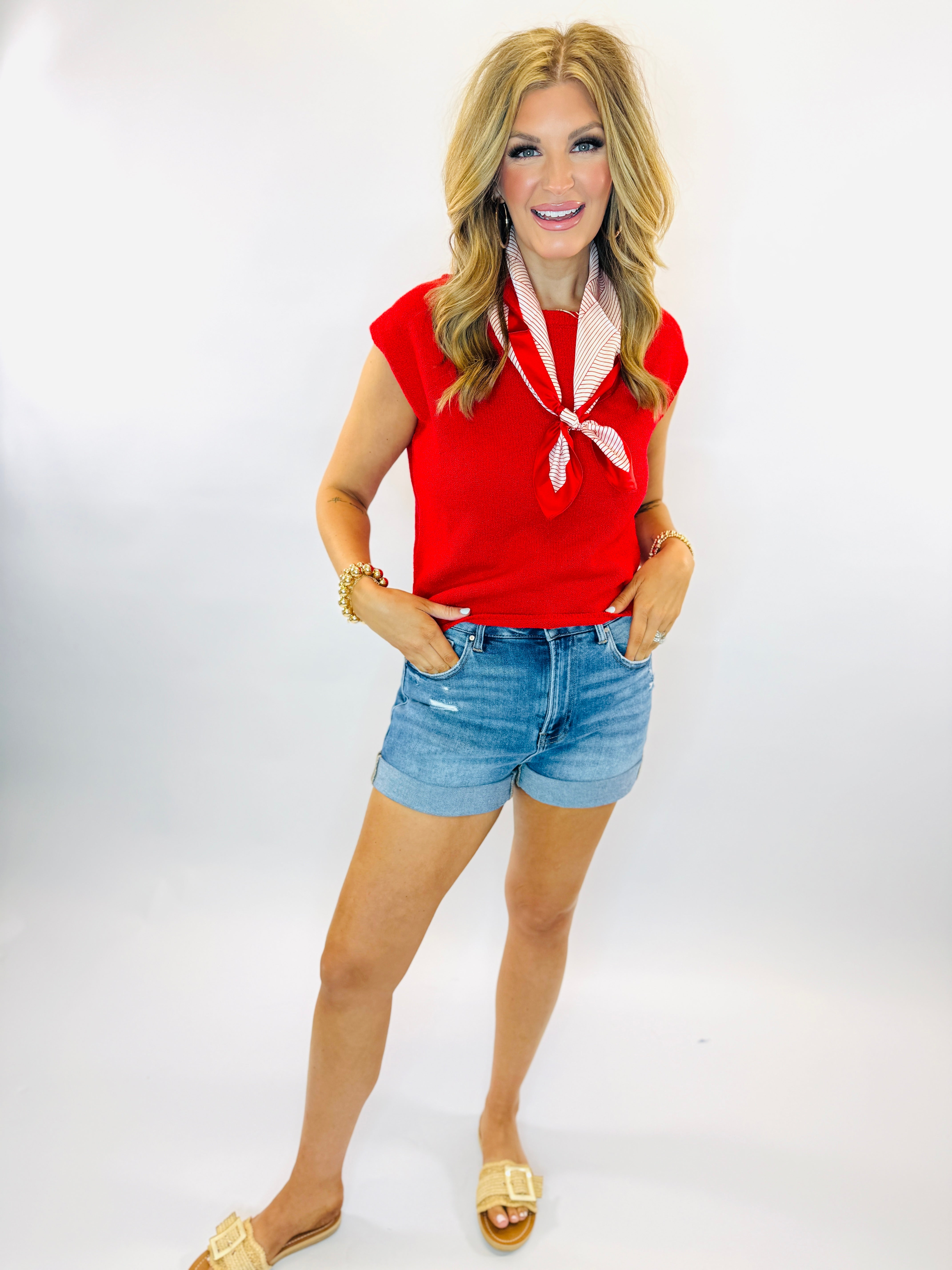 Woman wearing red sleeveless Pam sweater top with striped scarf, denim shorts, and gold sandals