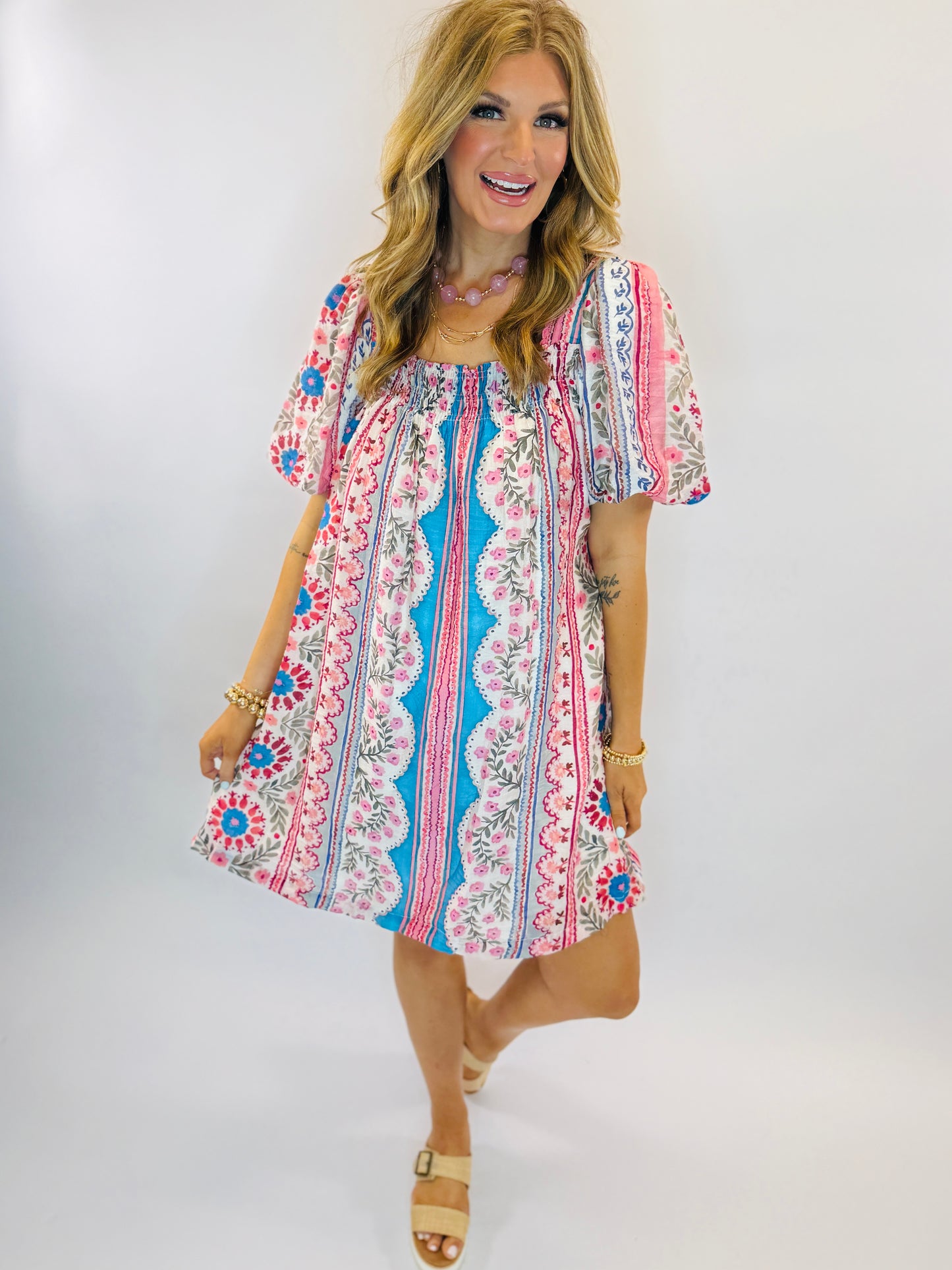 Woman wearing colorful floral patterned short-sleeve dress with blue, pink and white bohemian print design.