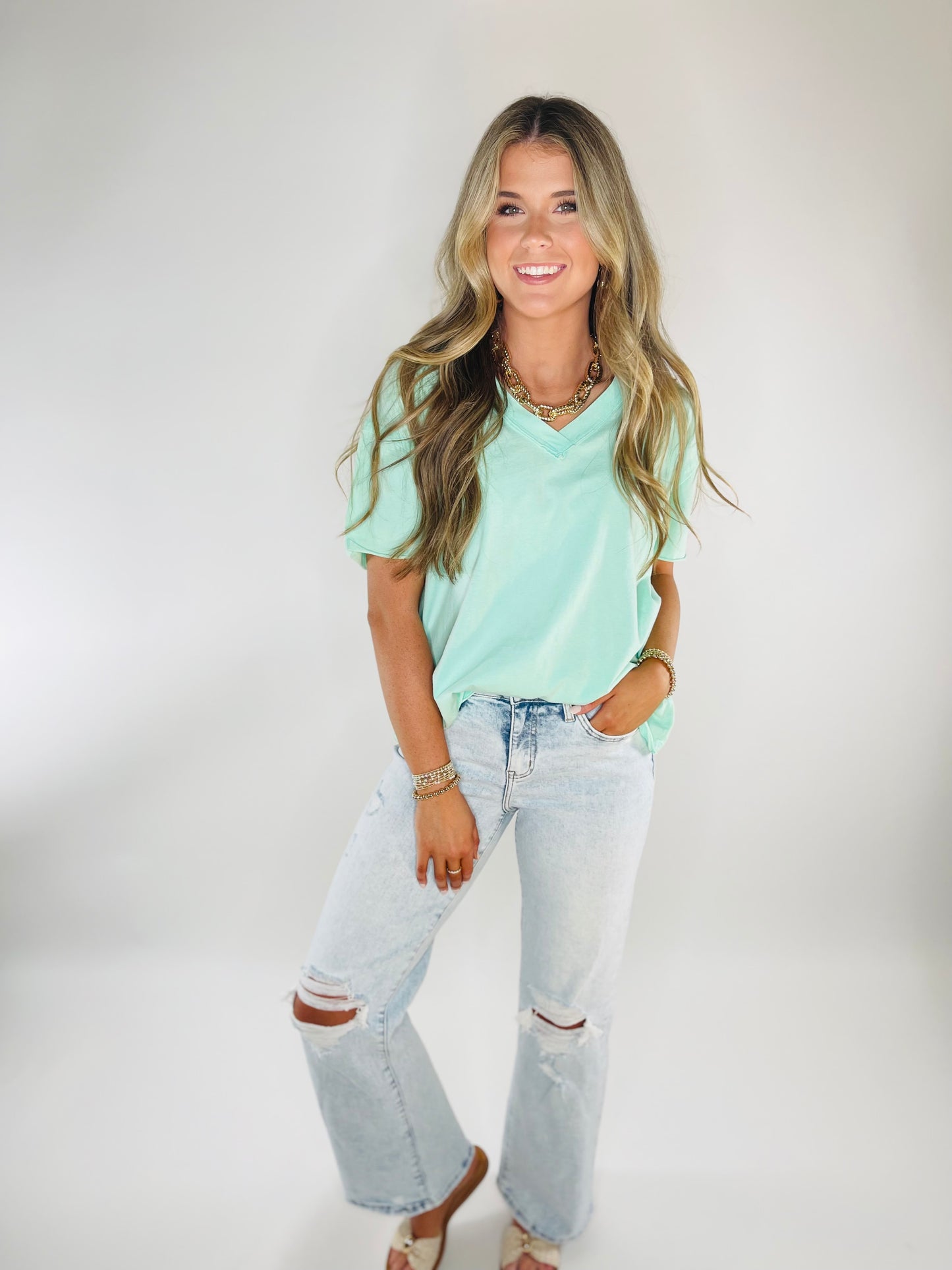 Woman wearing mint green Ailani v-neck tee with distressed light wash jeans and gold jewelry accessories.