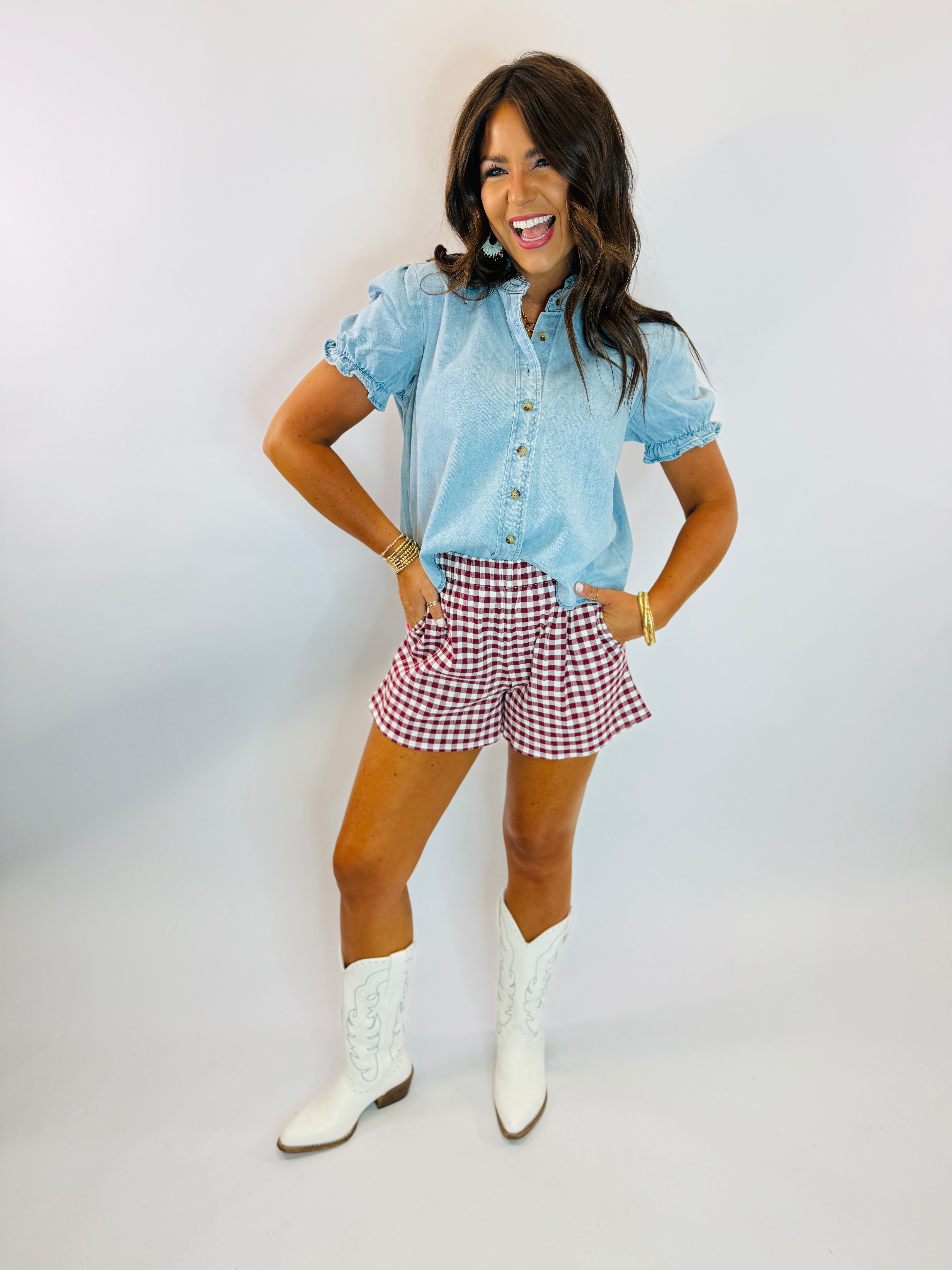 Woman wearing light blue chambray Warren Top with puff sleeves, paired with gingham shorts and white cowboy boots.