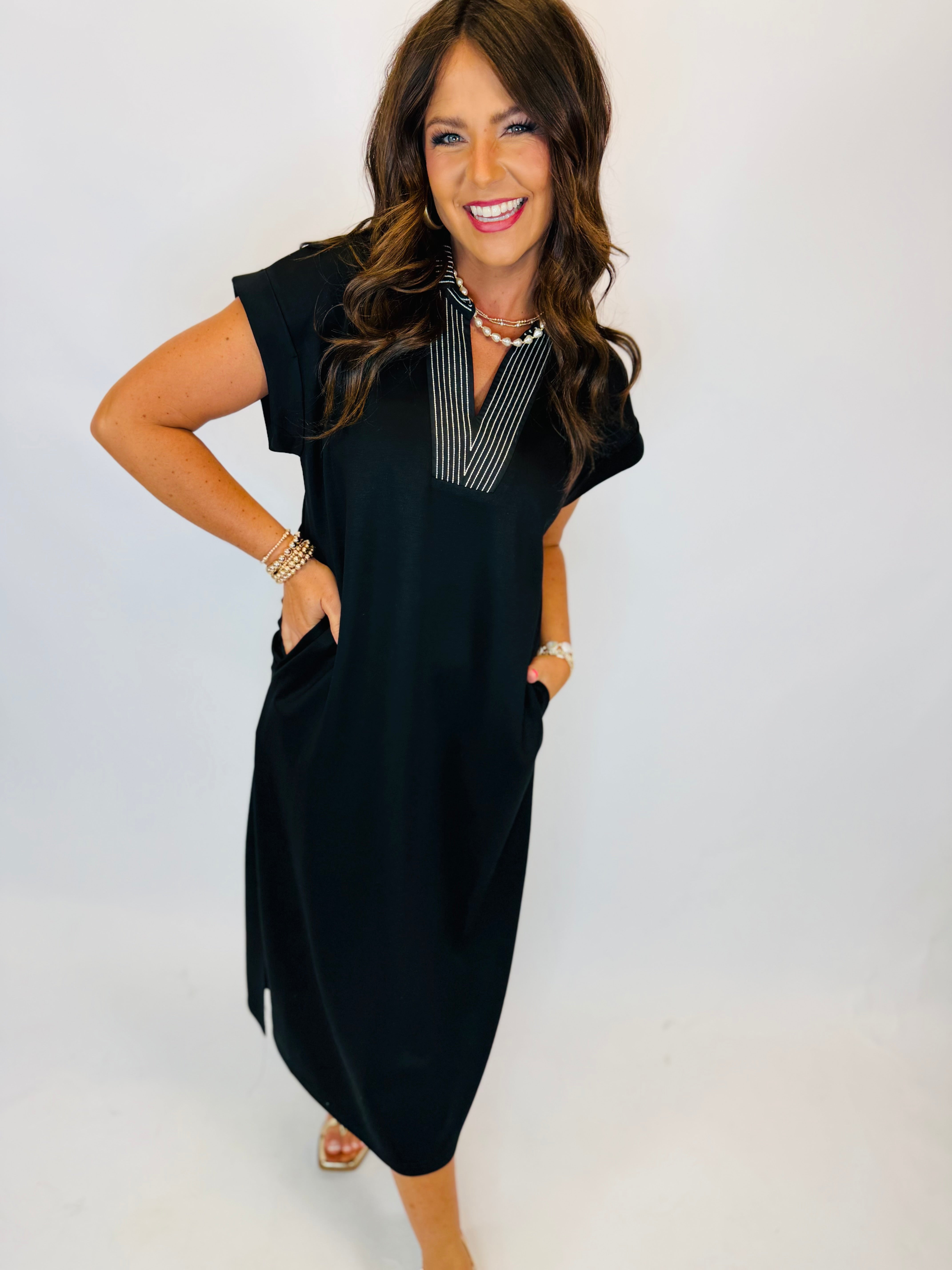 Black maxi dress with white striped V-neckline, short sleeves, and side pockets, modeled by woman with brown hair.