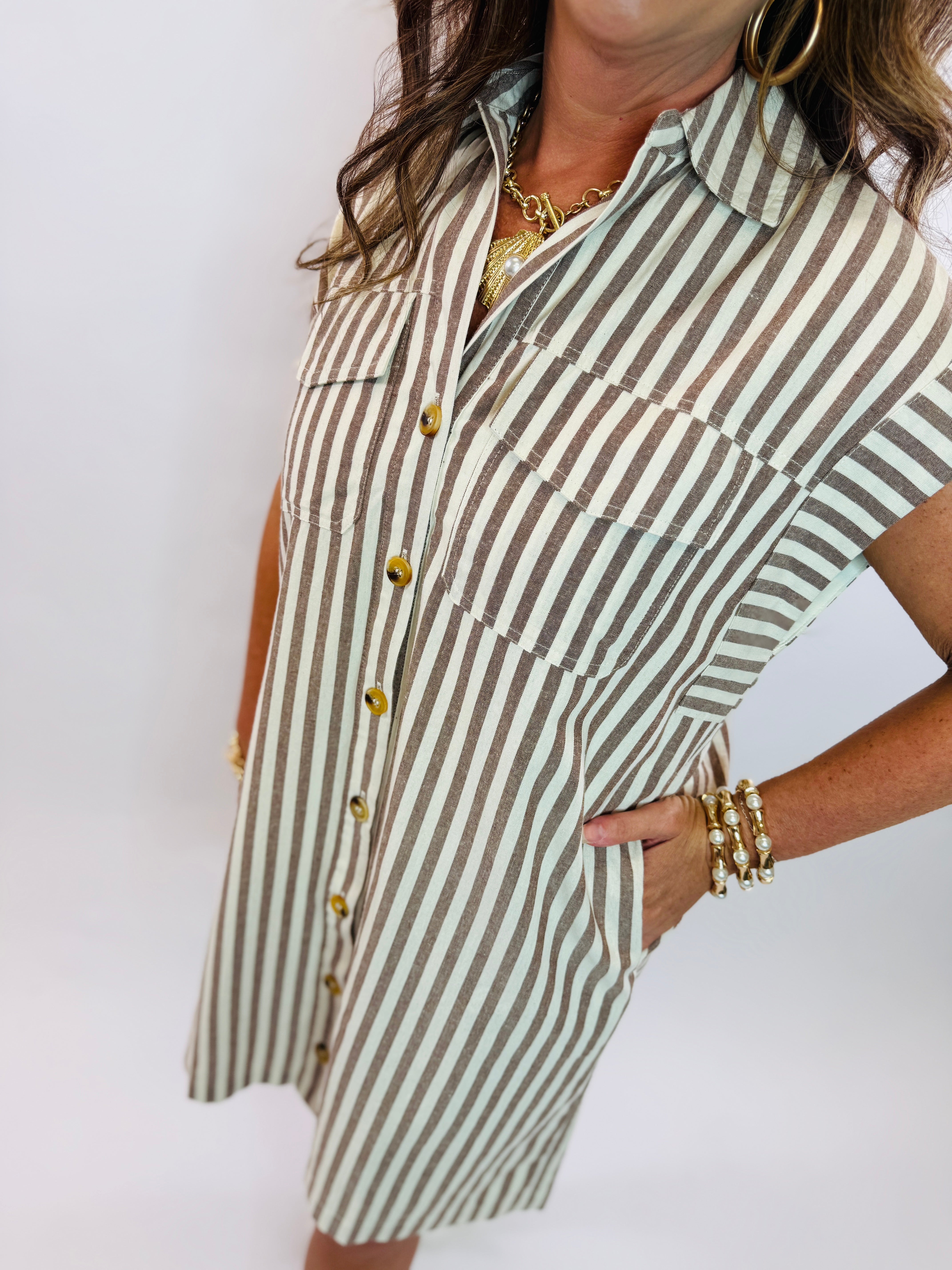 Woman wearing olive and white striped button-front shirt dress with gold jewelry and bracelets