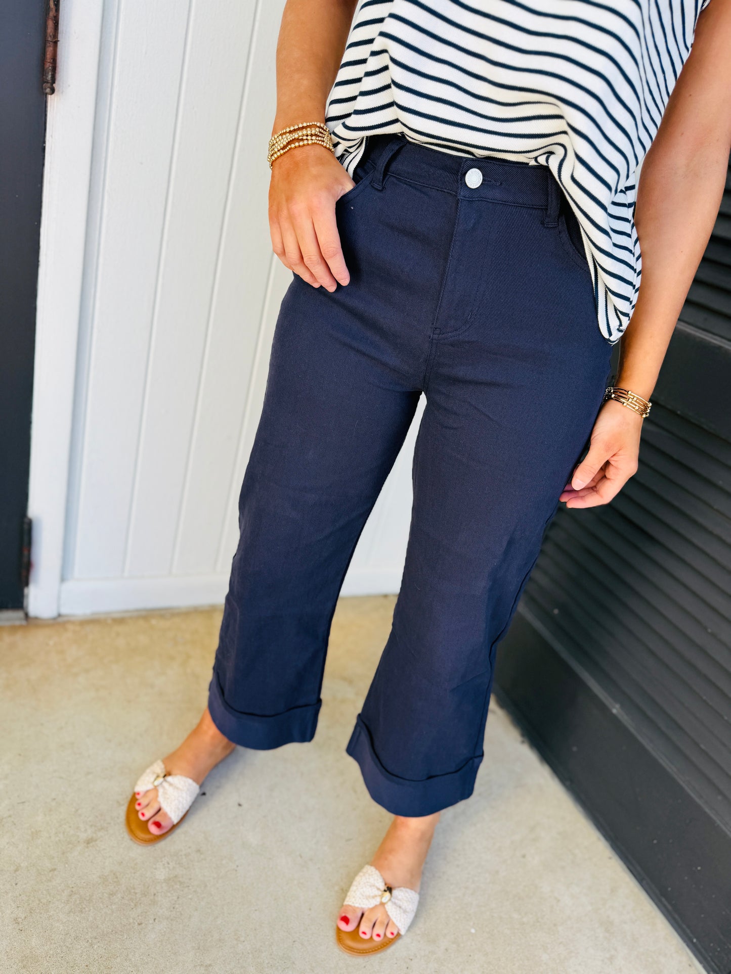 Woman wearing navy blue cuffed pants with striped top and white slide sandals