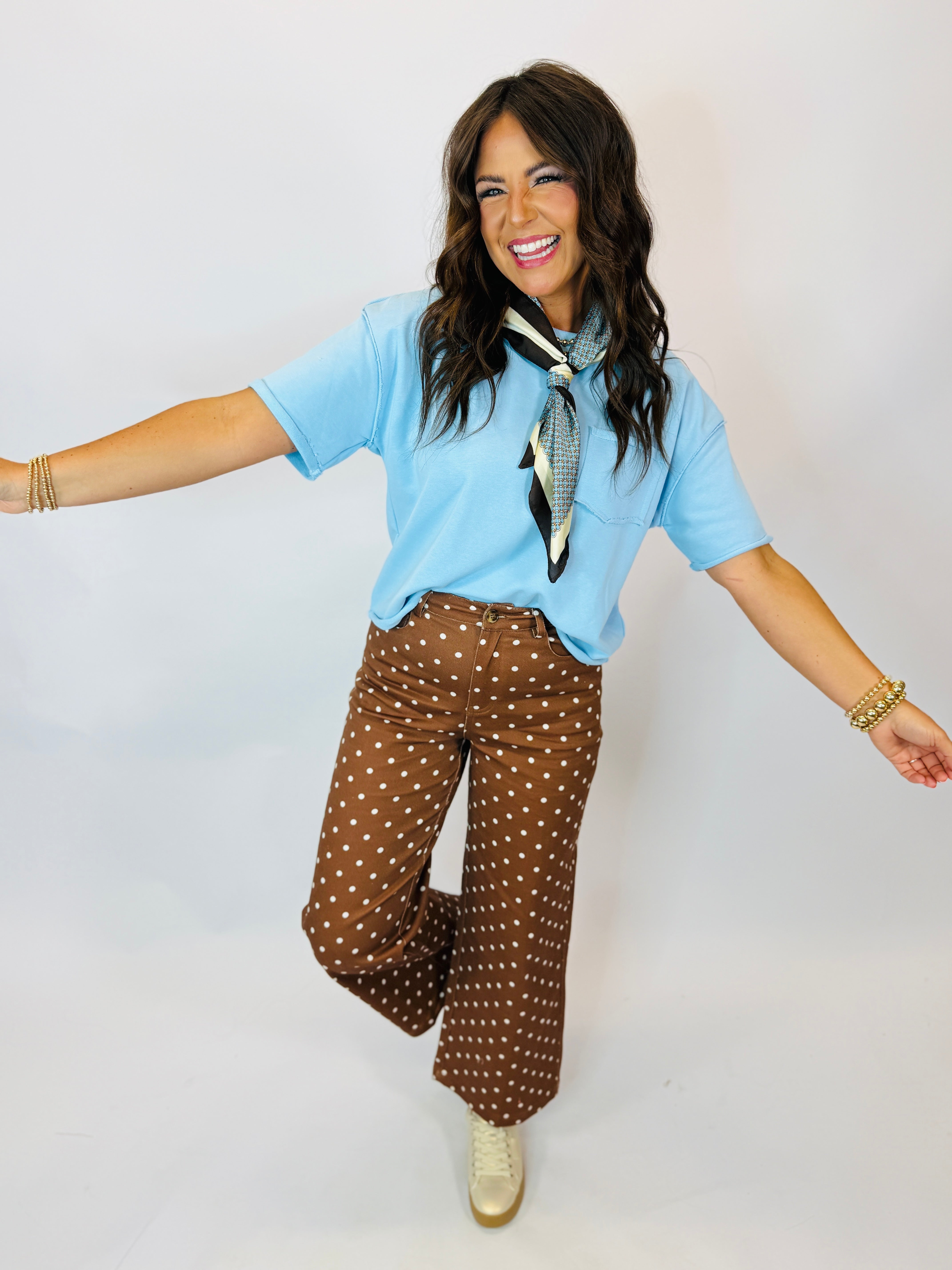 Woman wearing light blue short-sleeve Becka Top with neck scarf, paired with brown polka dot wide-leg pants.