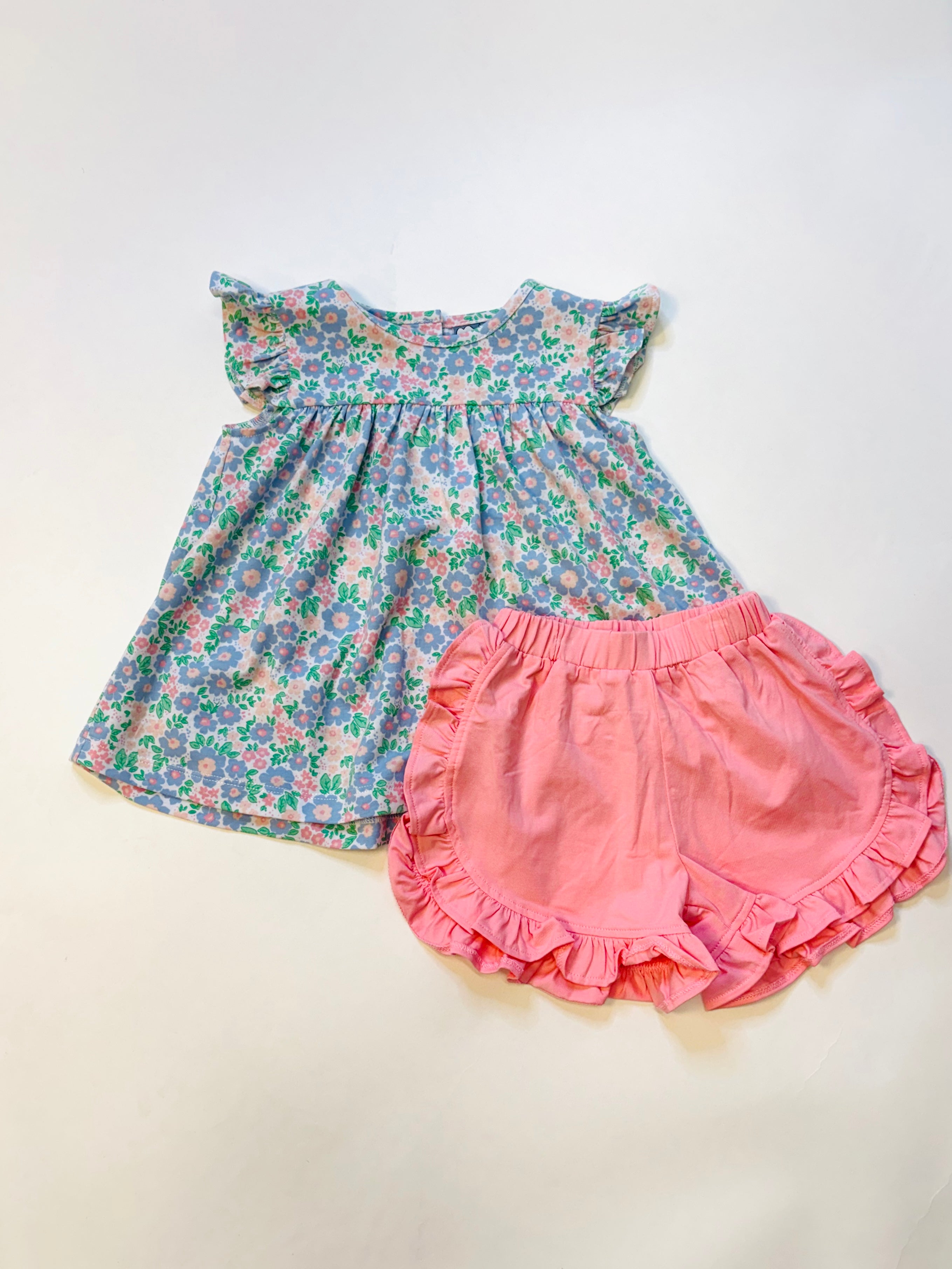 Floral sleeveless baby dress with ruffled shoulders paired with coral pink ruffled shorts on white background.