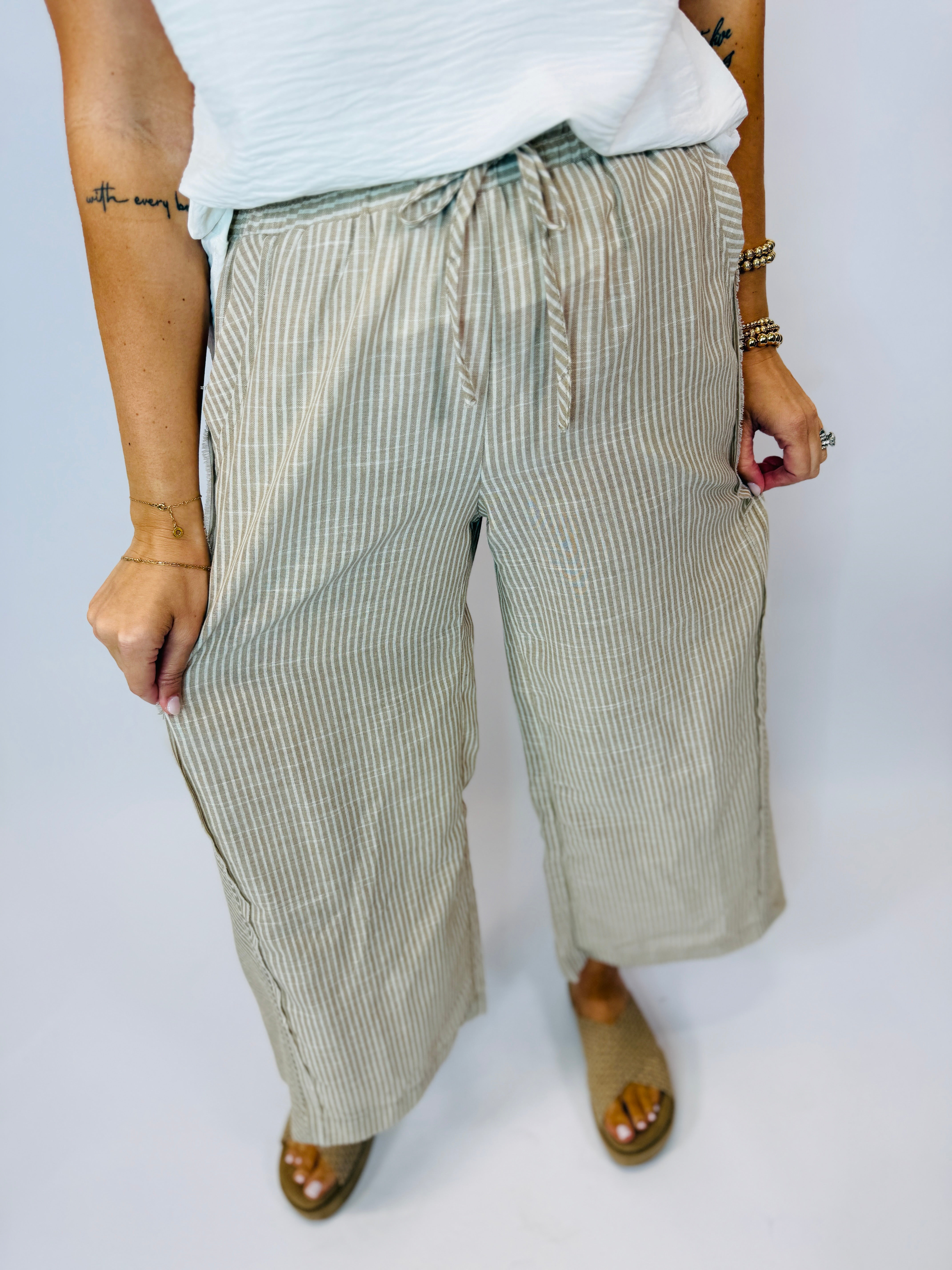 Woman wearing sage green and white striped wide-leg drawstring pants with white top and brown sandals.