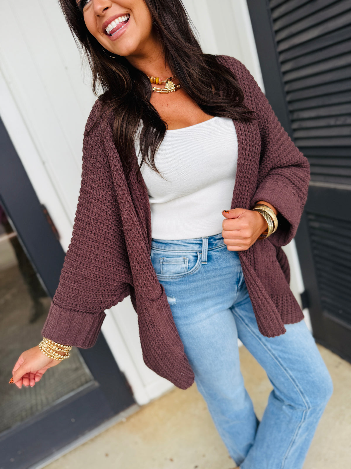 Woman wearing white Sonia top with burgundy knit cardigan and light blue jeans, styled with gold jewelry.