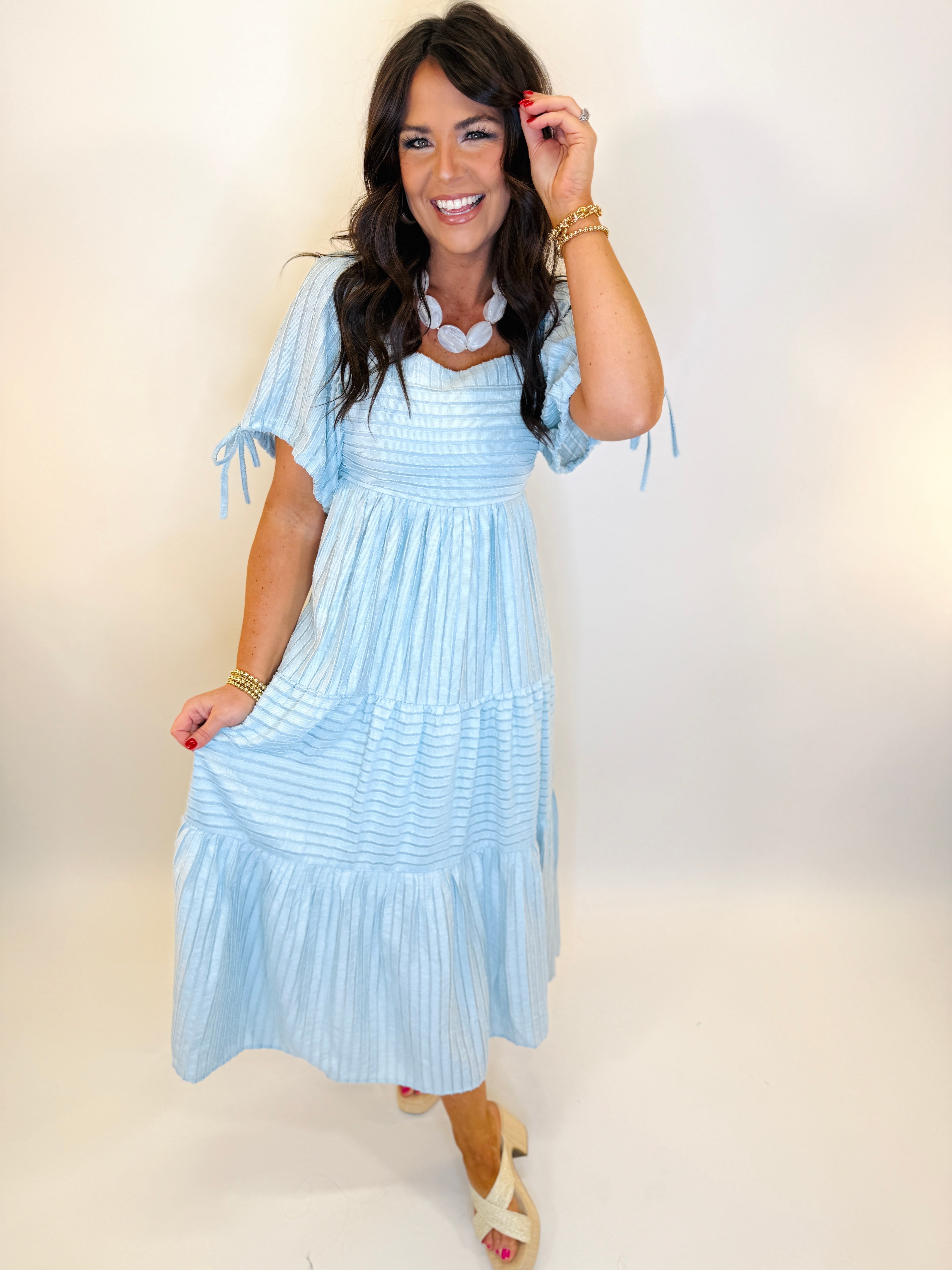 Woman wearing light blue tiered maxi dress with short sleeves and smocked bodice, styled with gold jewelry