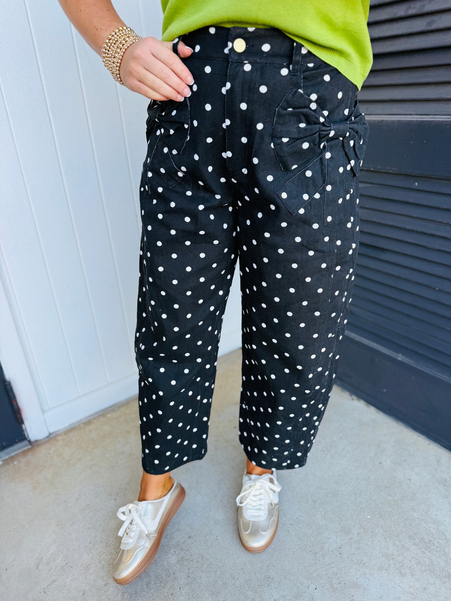 Black polka dot textured pants with tie waist detail, worn with lime green top and gold sneakers.