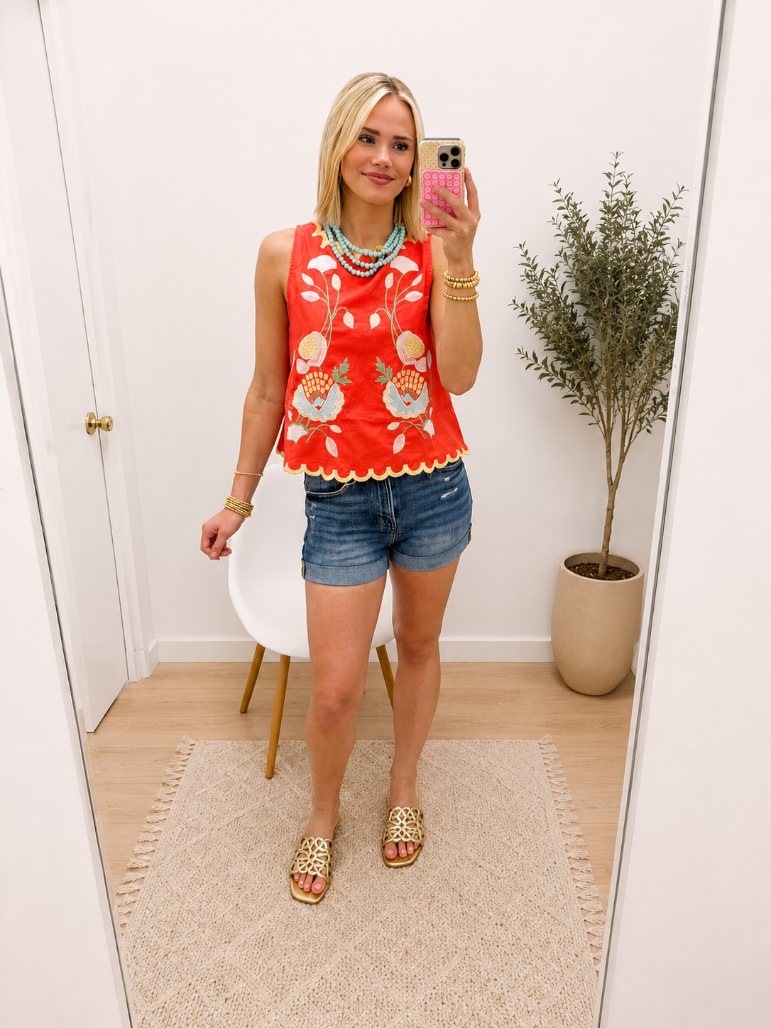 Woman wearing red sleeveless floral embroidered Alexa Top with scalloped hem, paired with denim shorts.