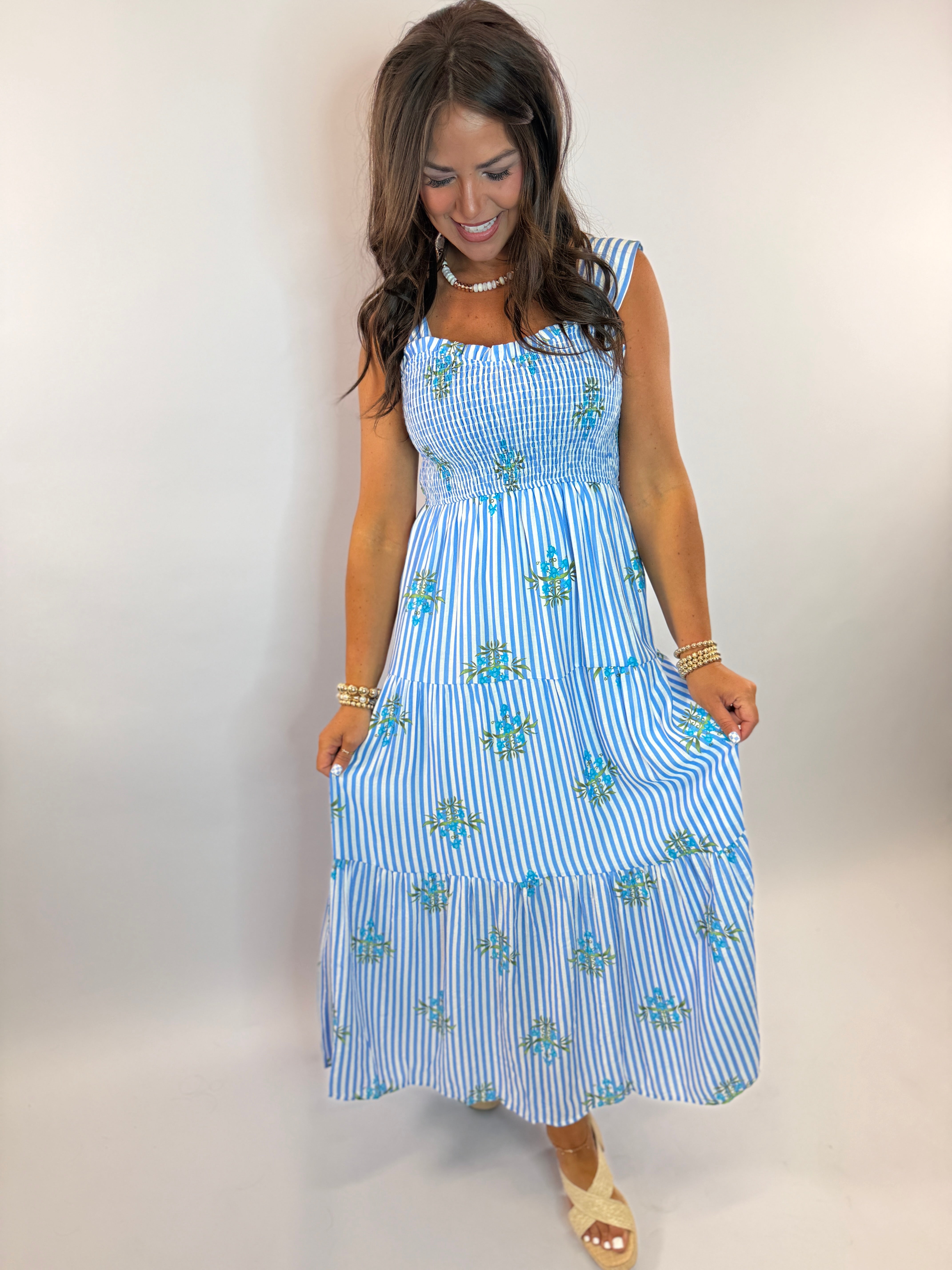 Blue and white striped maxi dress with smocked bodice and floral embroidery, modeled by woman with pearl necklace.