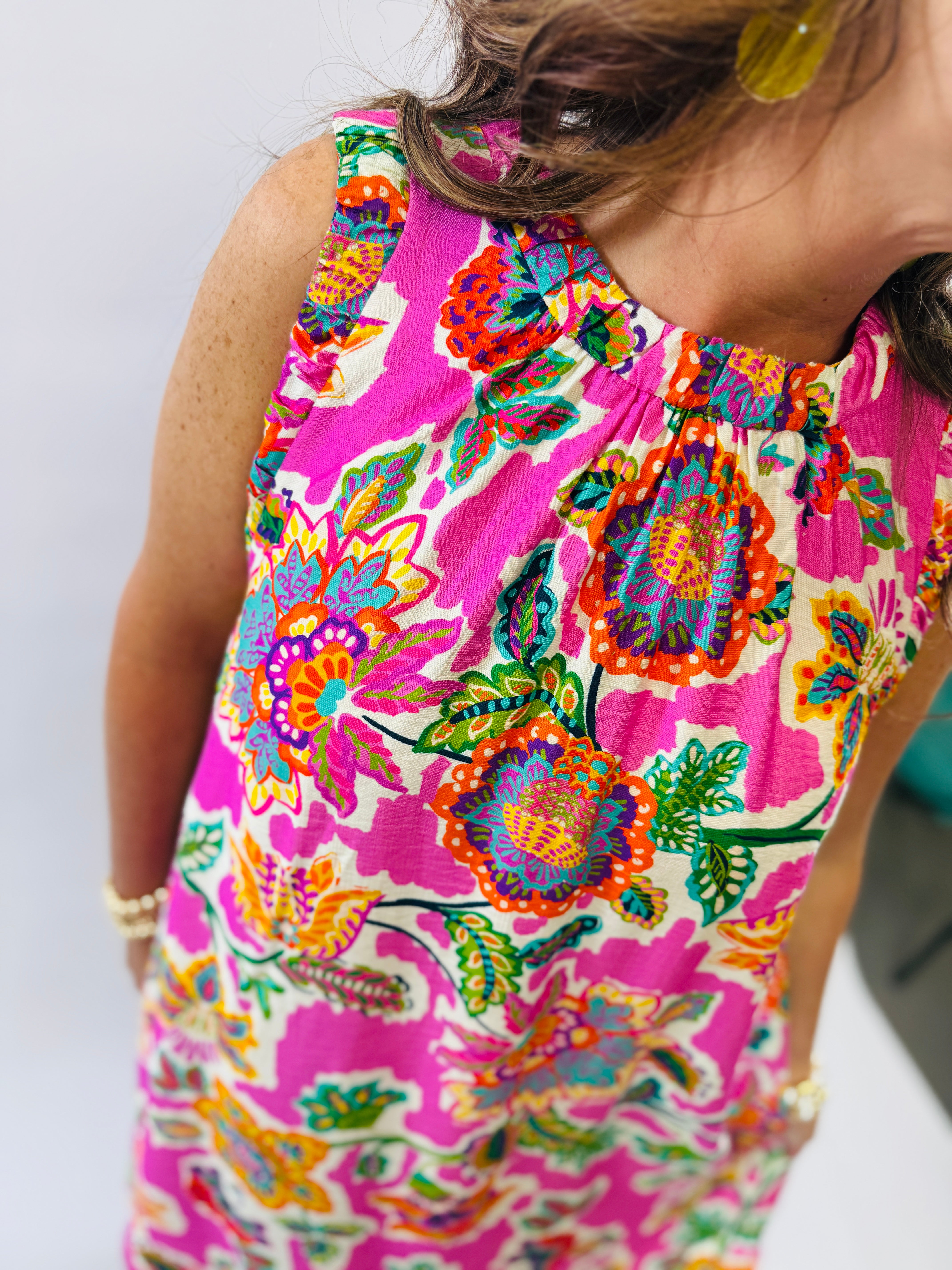 Colorful sleeveless Lilly dress with vibrant pink and multicolored floral pattern, featuring ruffled neckline detail.