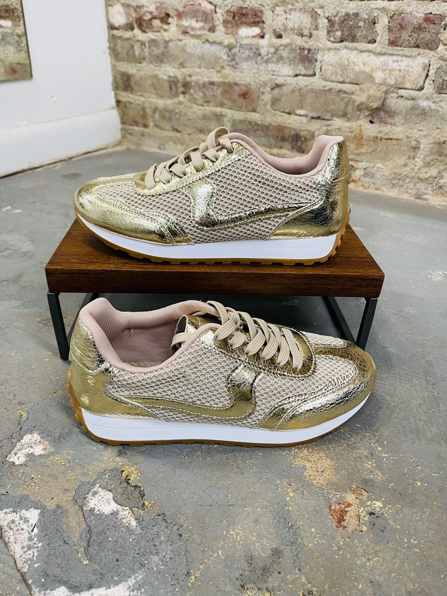 Gold metallic Griffin sneakers with mesh detailing and white soles displayed on wooden platform