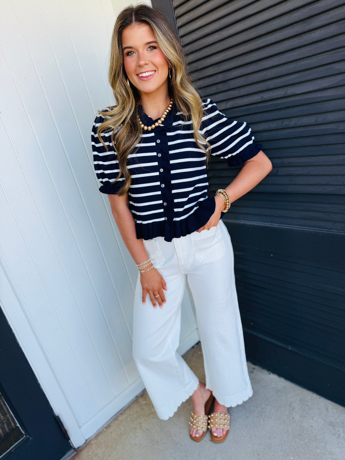Woman wearing navy and white striped button-up cardigan with white wide-leg pants and gold jewelry.