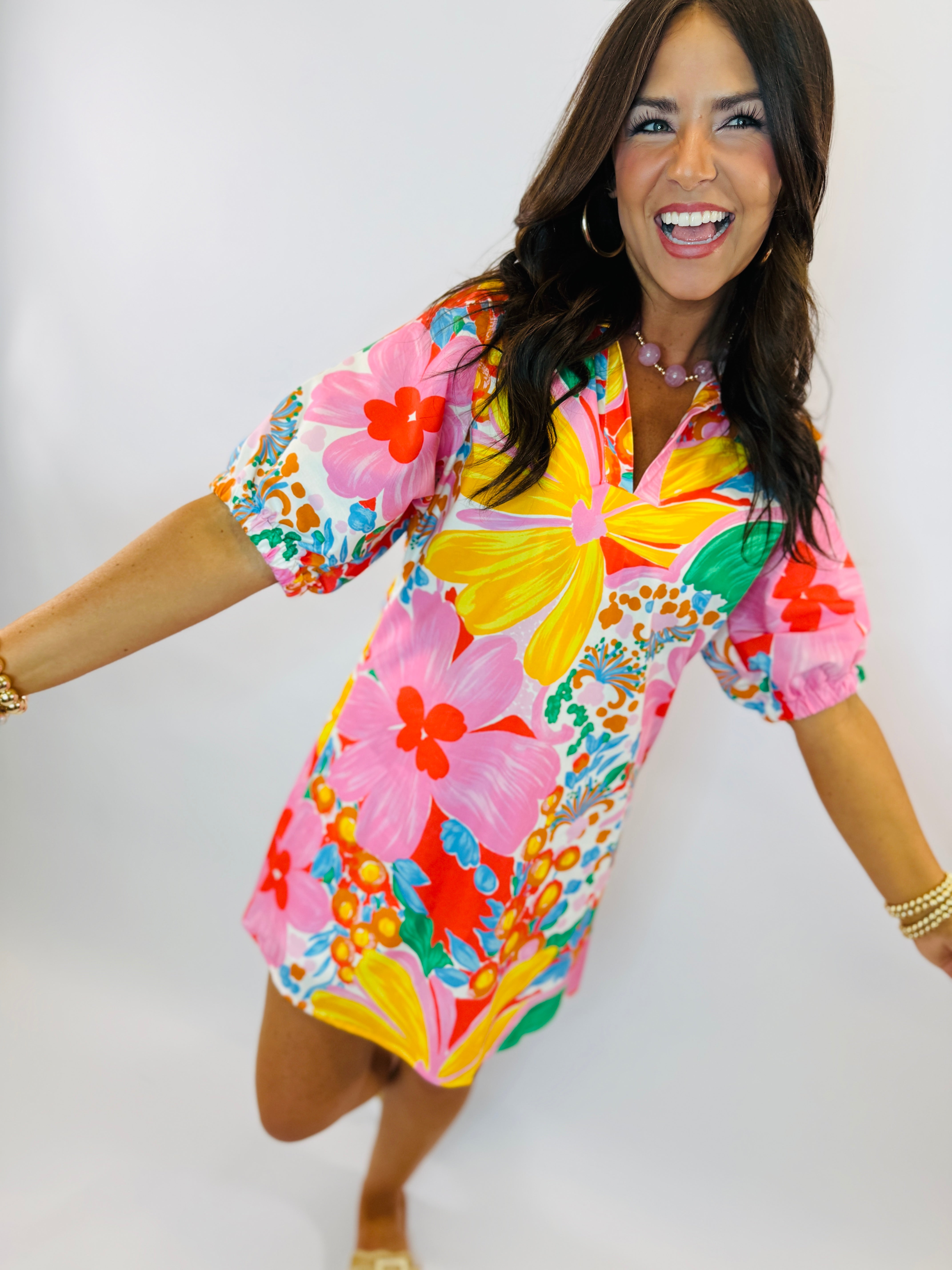 Woman wearing colorful tropical floral print dress with puffy sleeves, smiling and posing against white background.