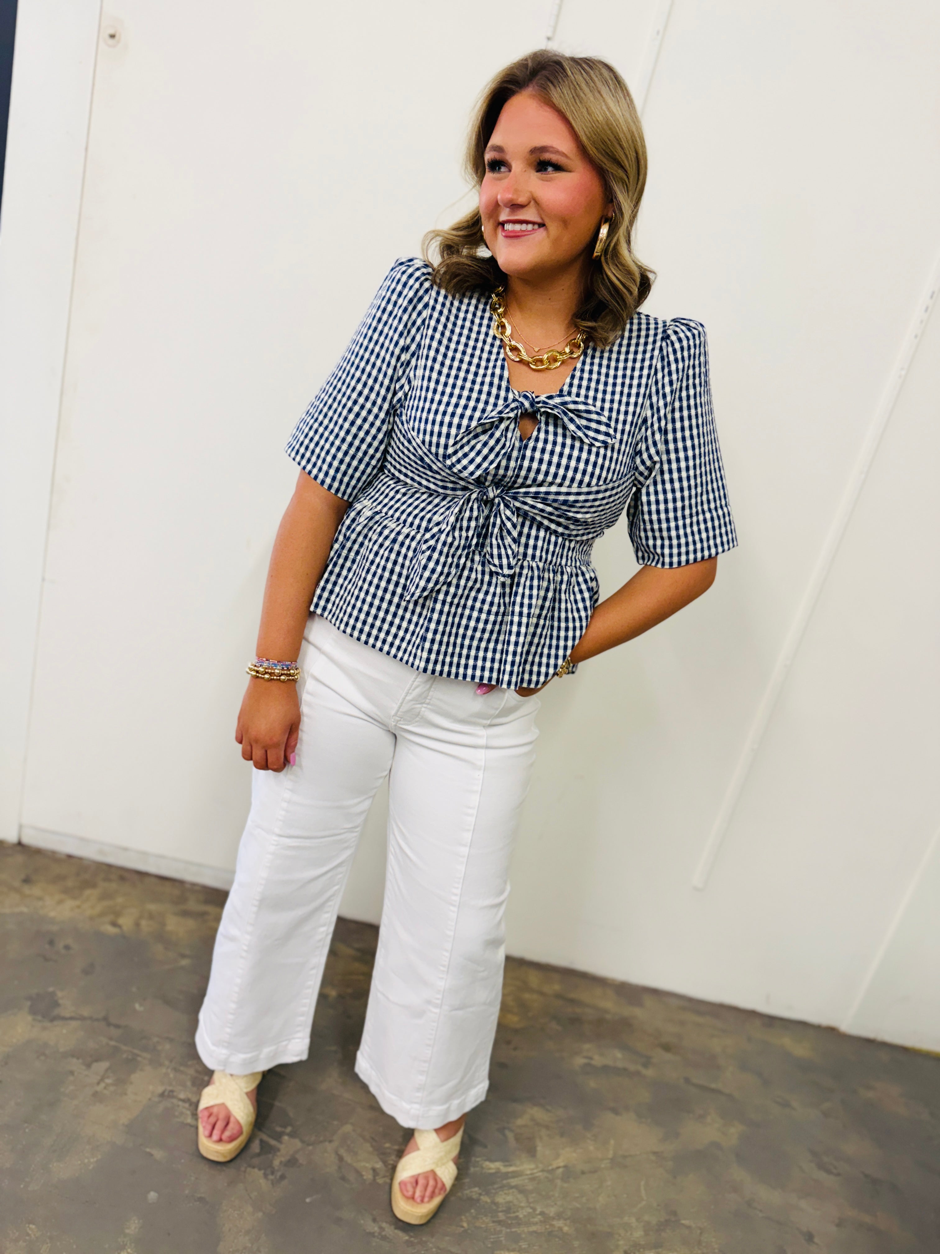 Woman wearing blue and white gingham checked flowy top with tie-front detail and white wide-leg pants