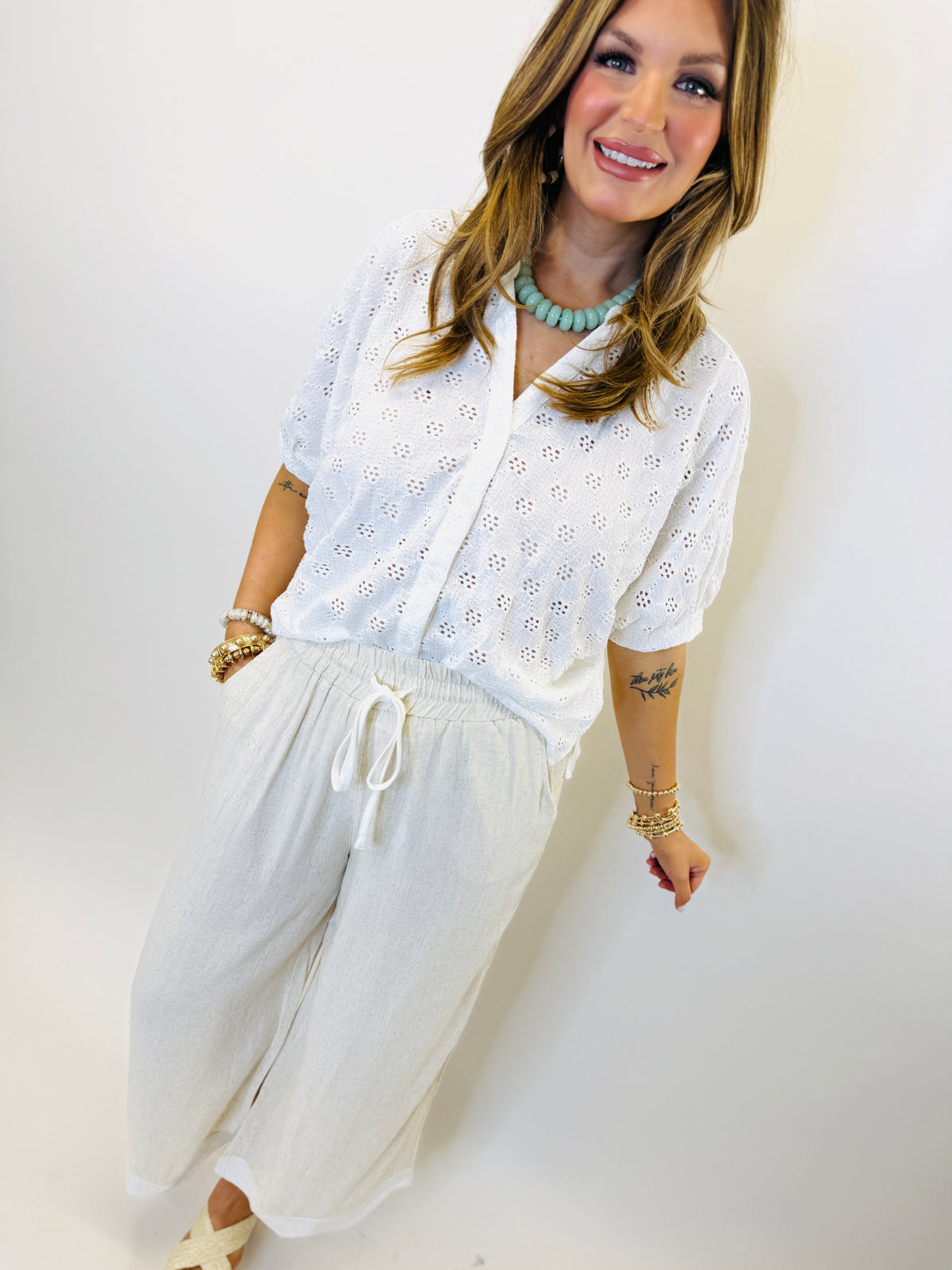 Woman wearing white eyelet lace short-sleeve button-up top with drawstring pants and turquoise necklace