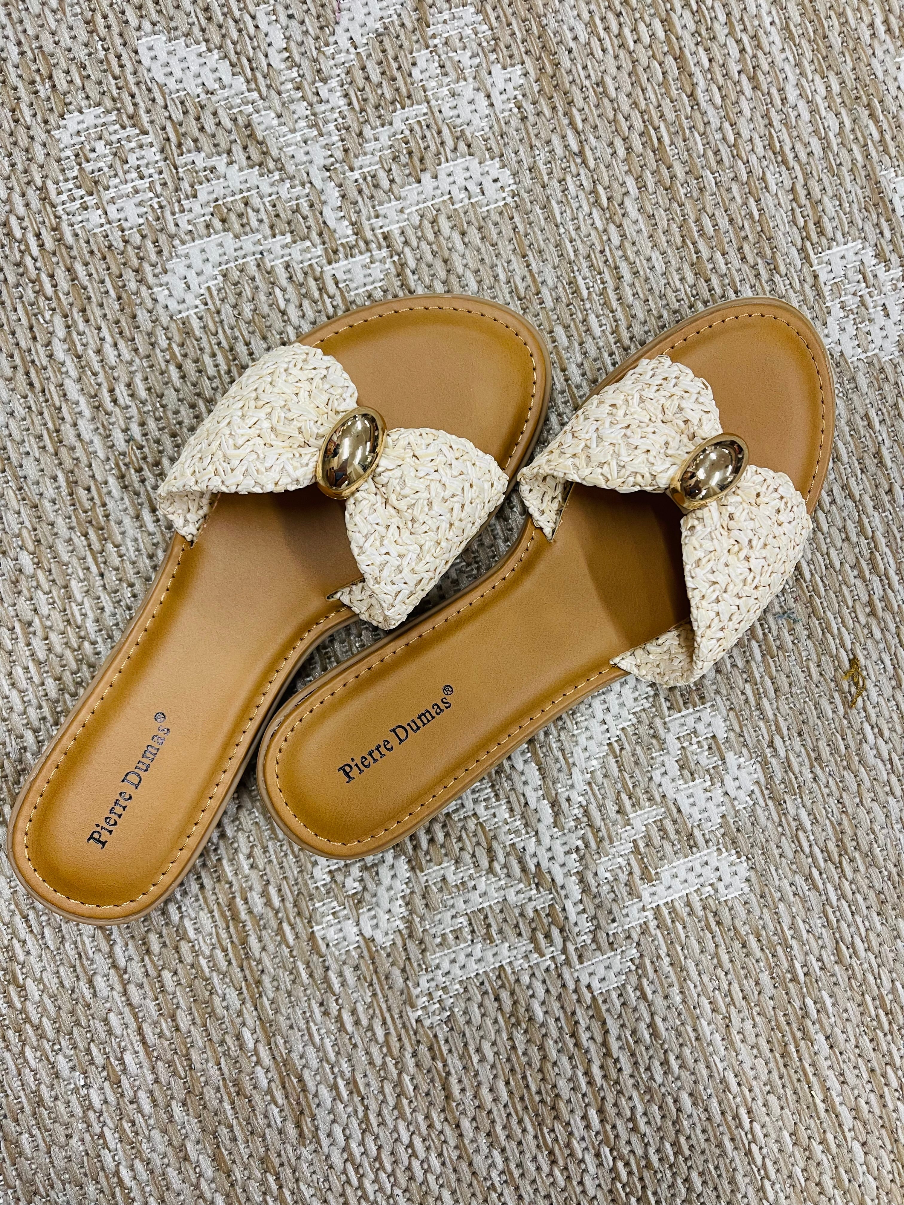 Cream woven slide sandals with gold buckle detail and tan leather footbed on textured fabric background