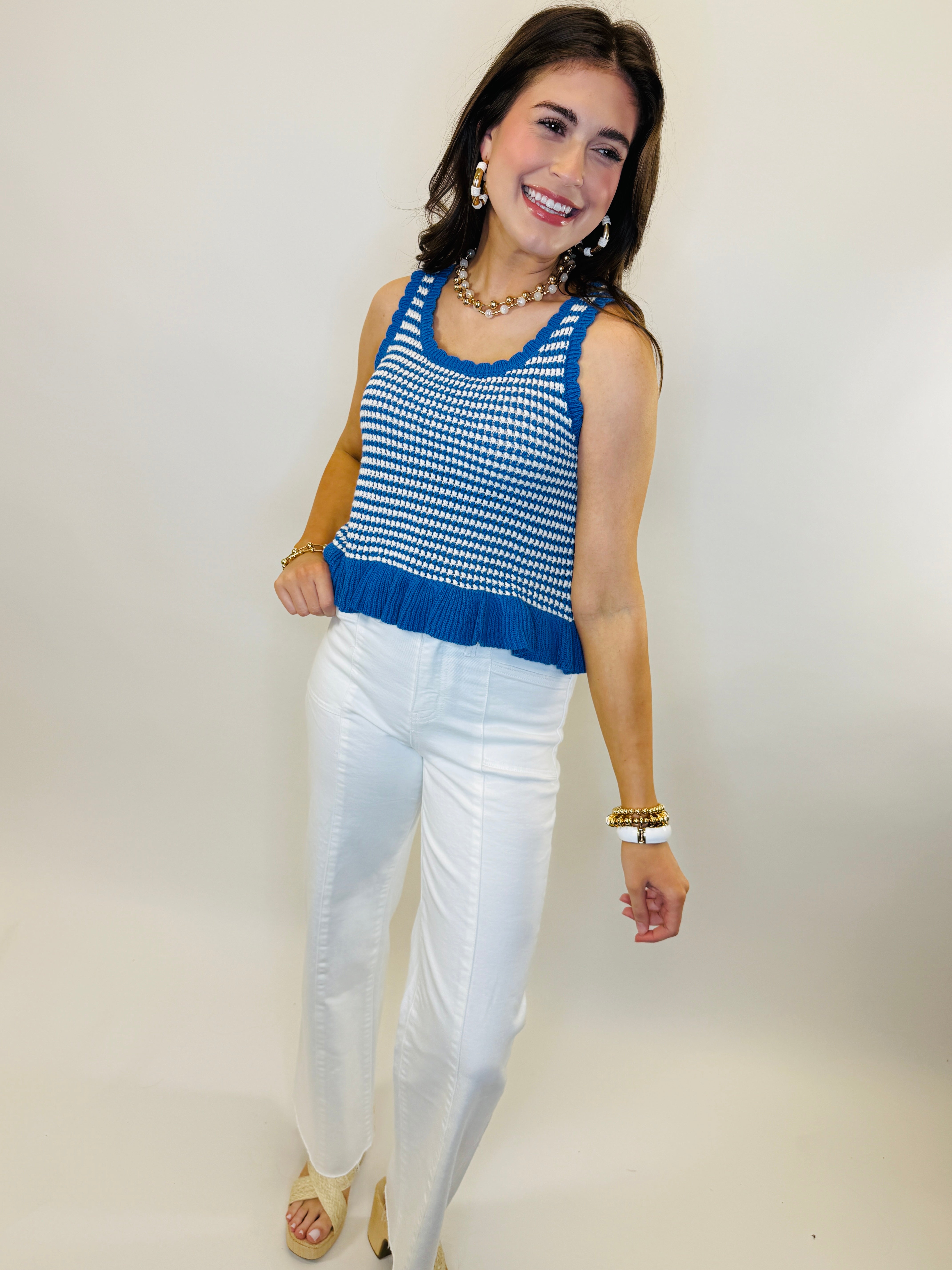 Woman wearing blue and white patterned knit tank top with white pants and gold jewelry accessories.