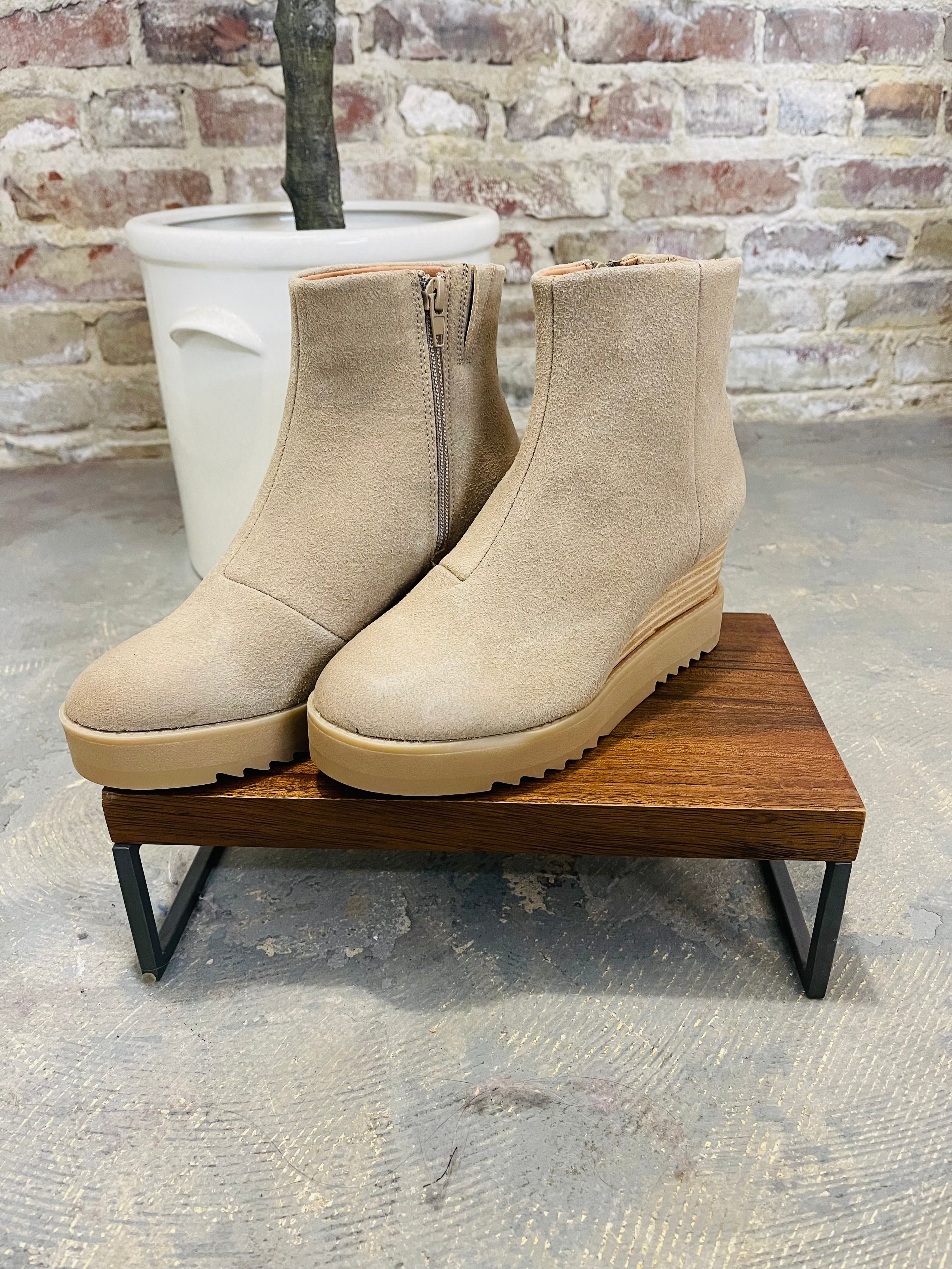 Beige suede ankle boots with platform soles and side zippers displayed on wooden bench