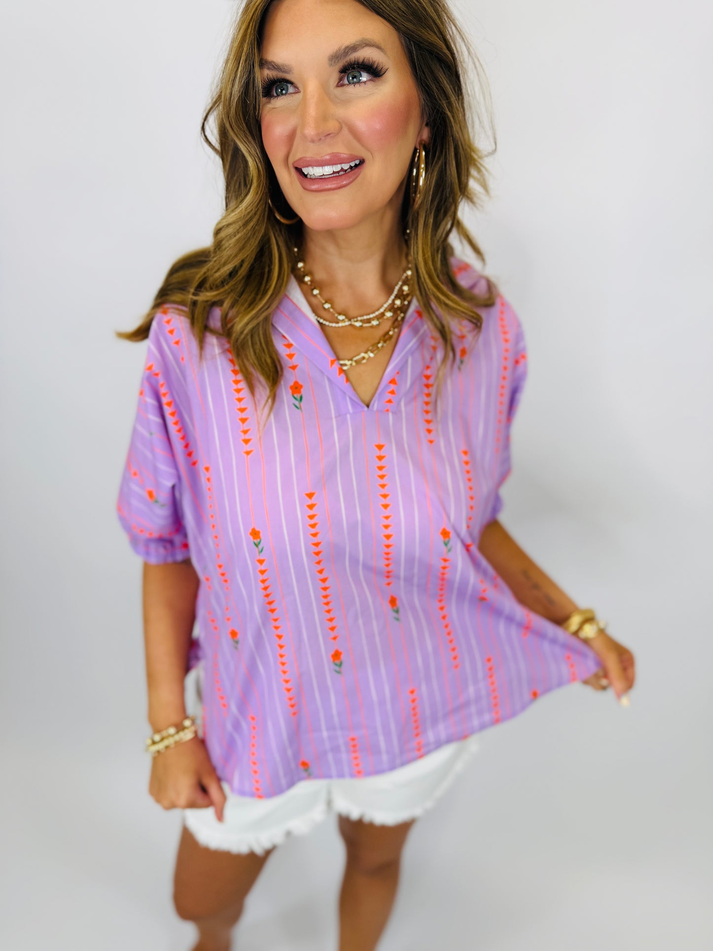 Woman wearing purple striped Sloan Top with red embroidered details and V-neckline, paired with white shorts.