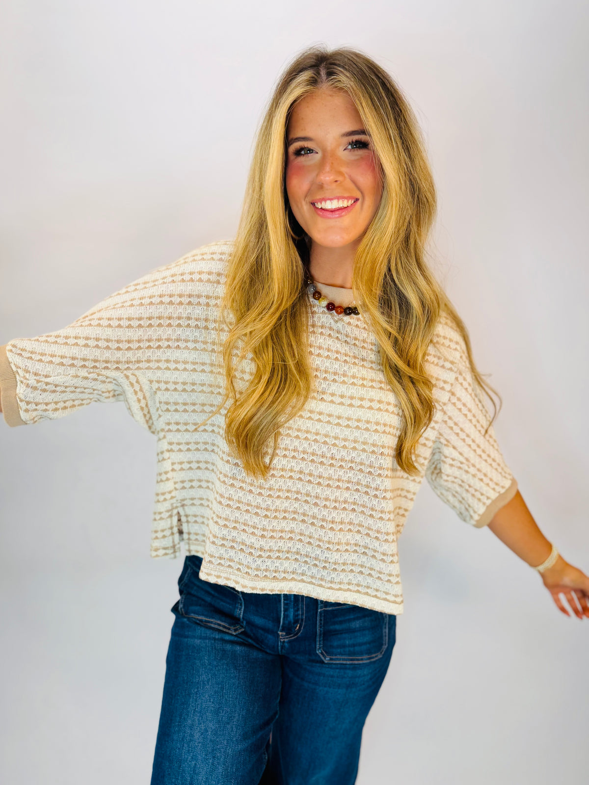 Cream and mocha striped open-knit sweater top with dolman sleeves, worn with dark jeans.
