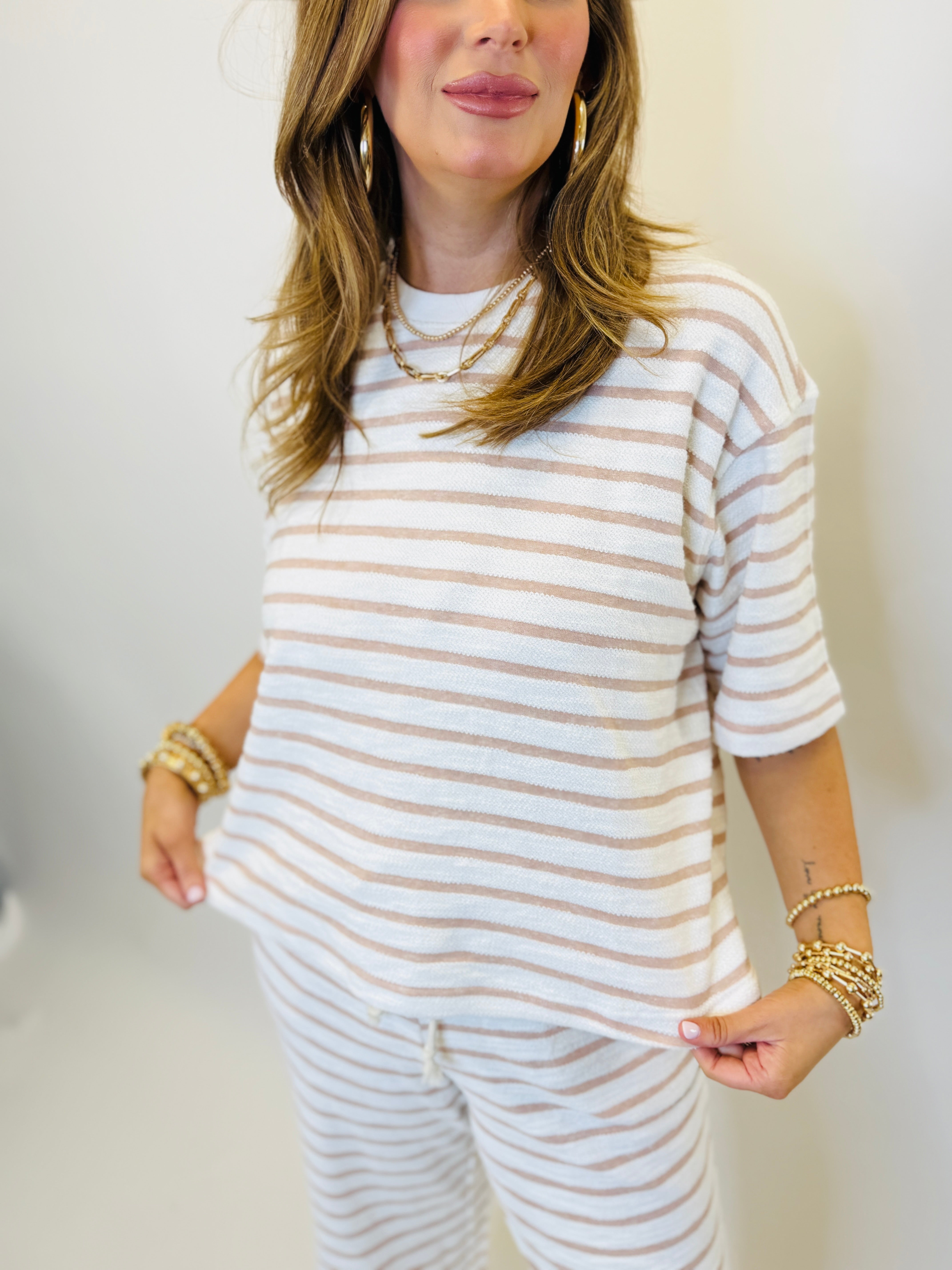 Woman wearing beige and white striped 3/4 sleeve top with matching striped pants and gold jewelry