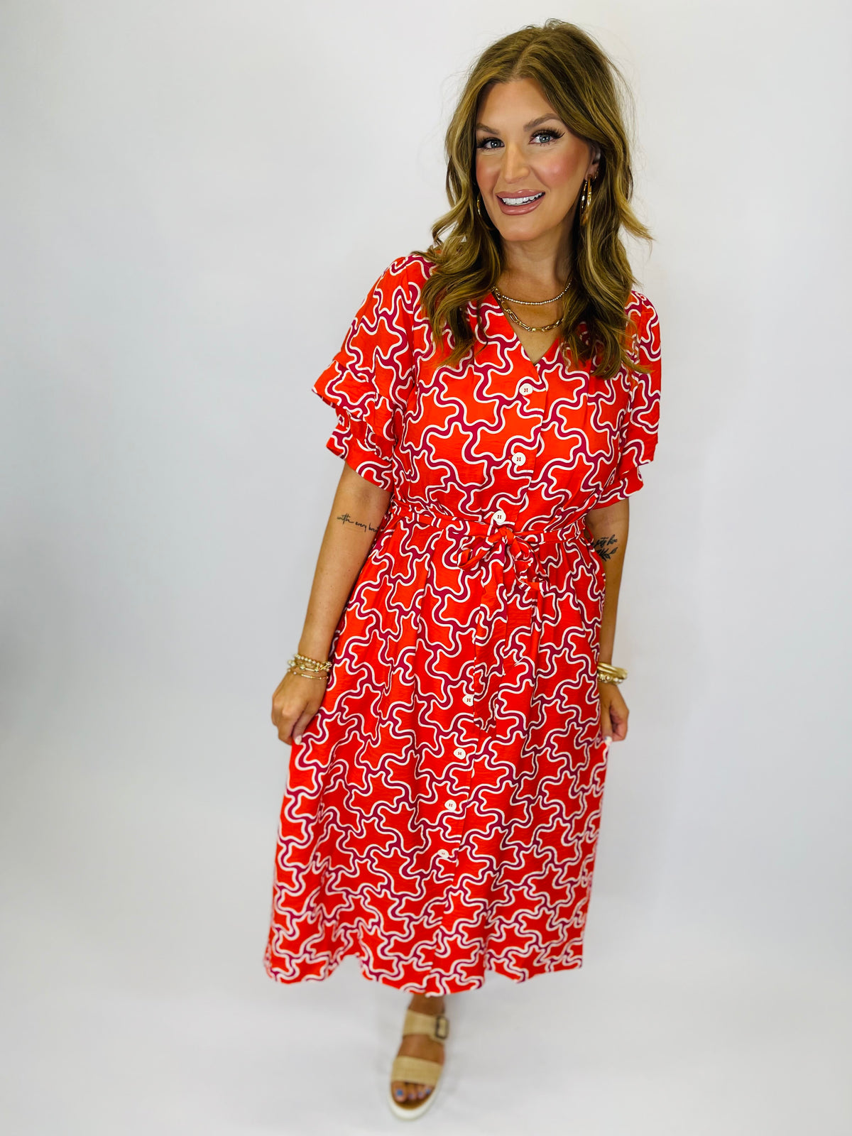 Woman wearing red and white patterned Cataleya midi dress with short sleeves and belt tie waist.