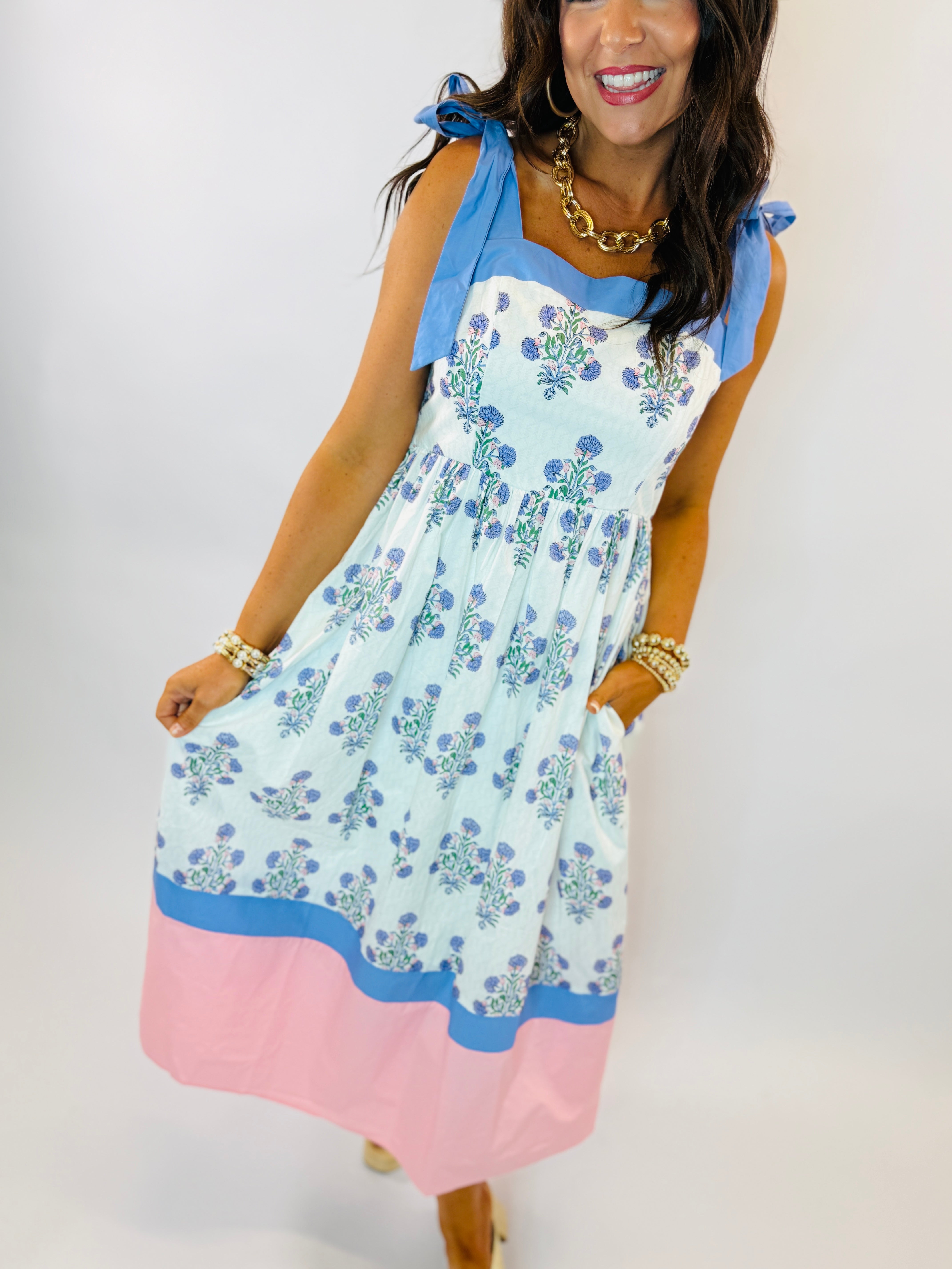 Woman wearing Jackie Dress with blue floral print, pink color block hem, and tie shoulder straps