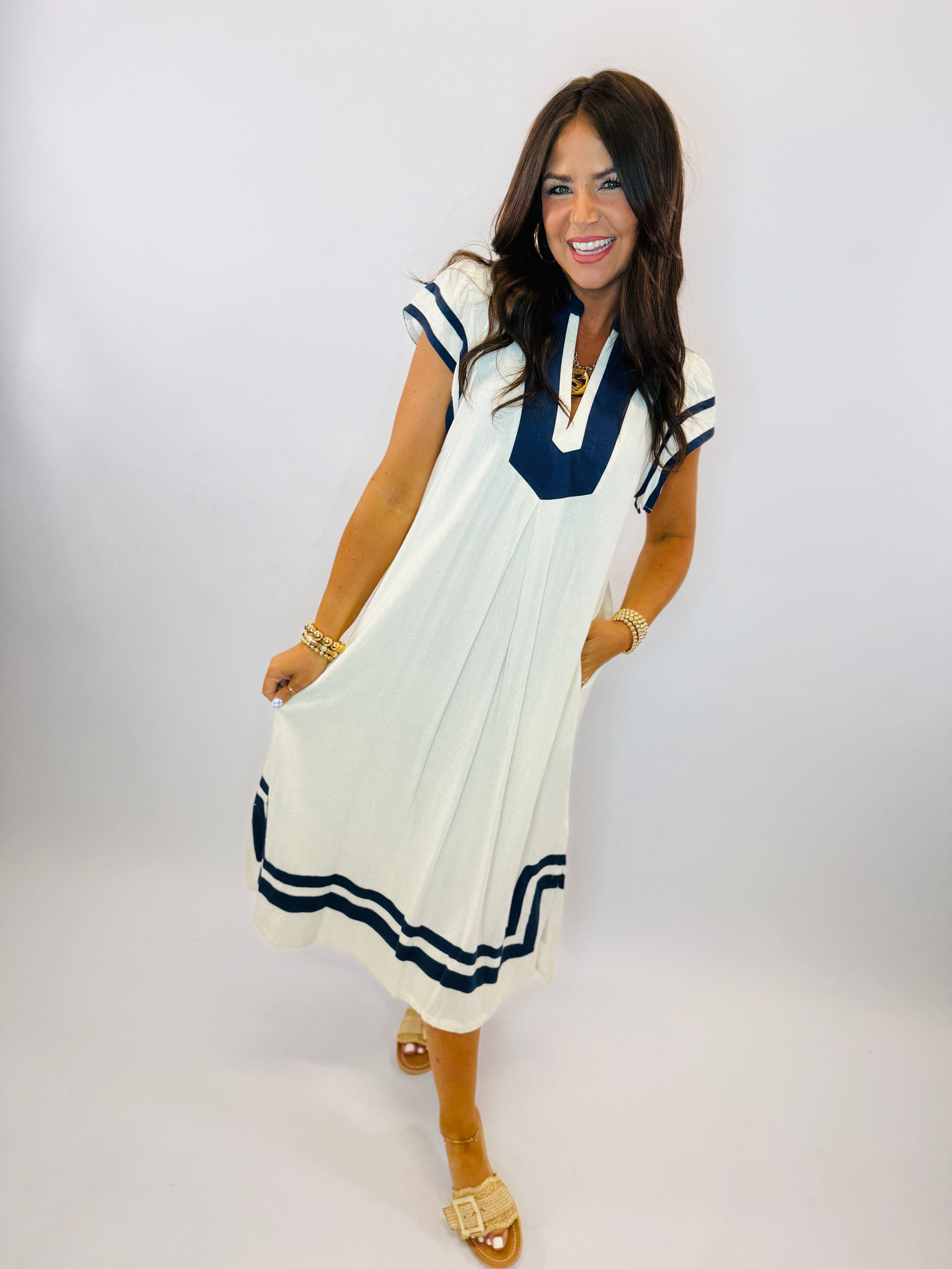 White midi dress with navy blue trim and cap sleeves, worn by smiling woman with gold accessories.