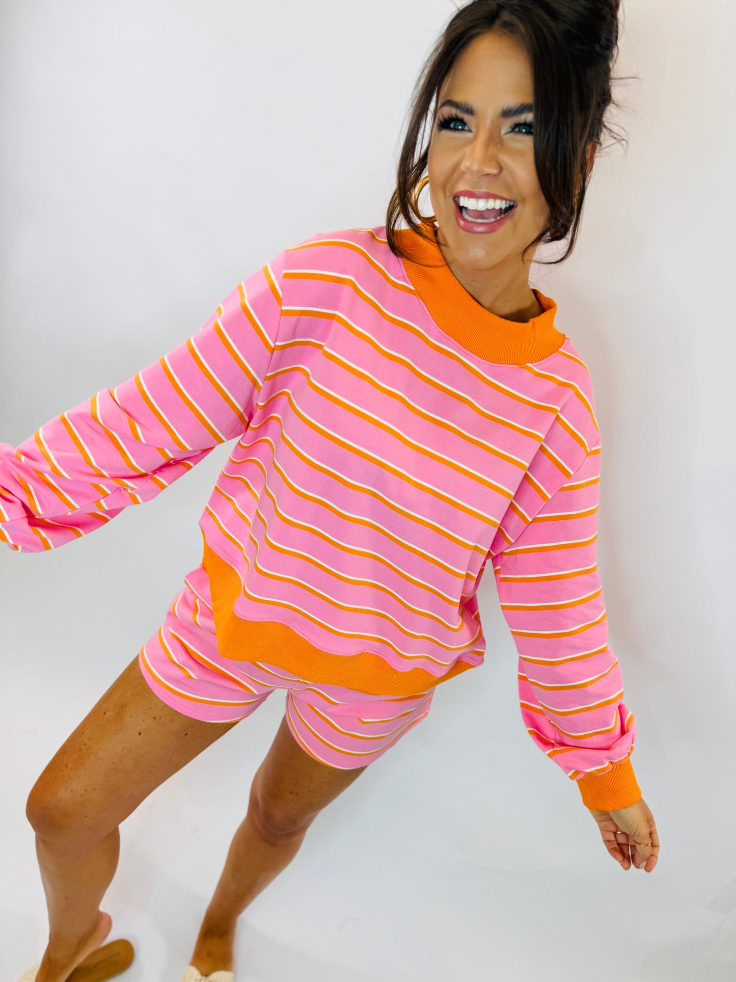 Woman wearing bright pink and orange striped long-sleeve top with matching shorts in playful pose