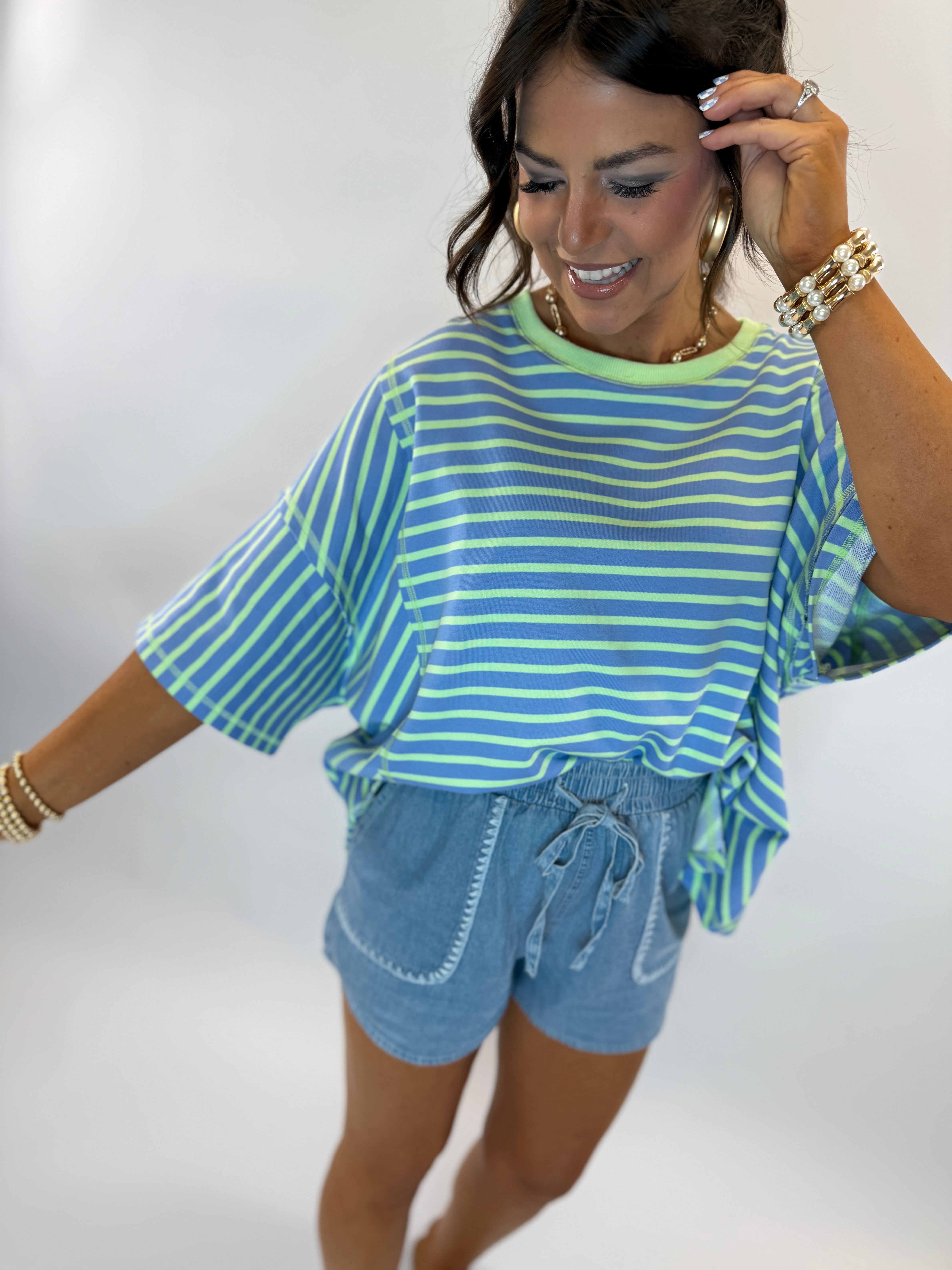 Woman wearing blue chambray drawstring shorts with white contrast stitching and pockets, paired with striped top.