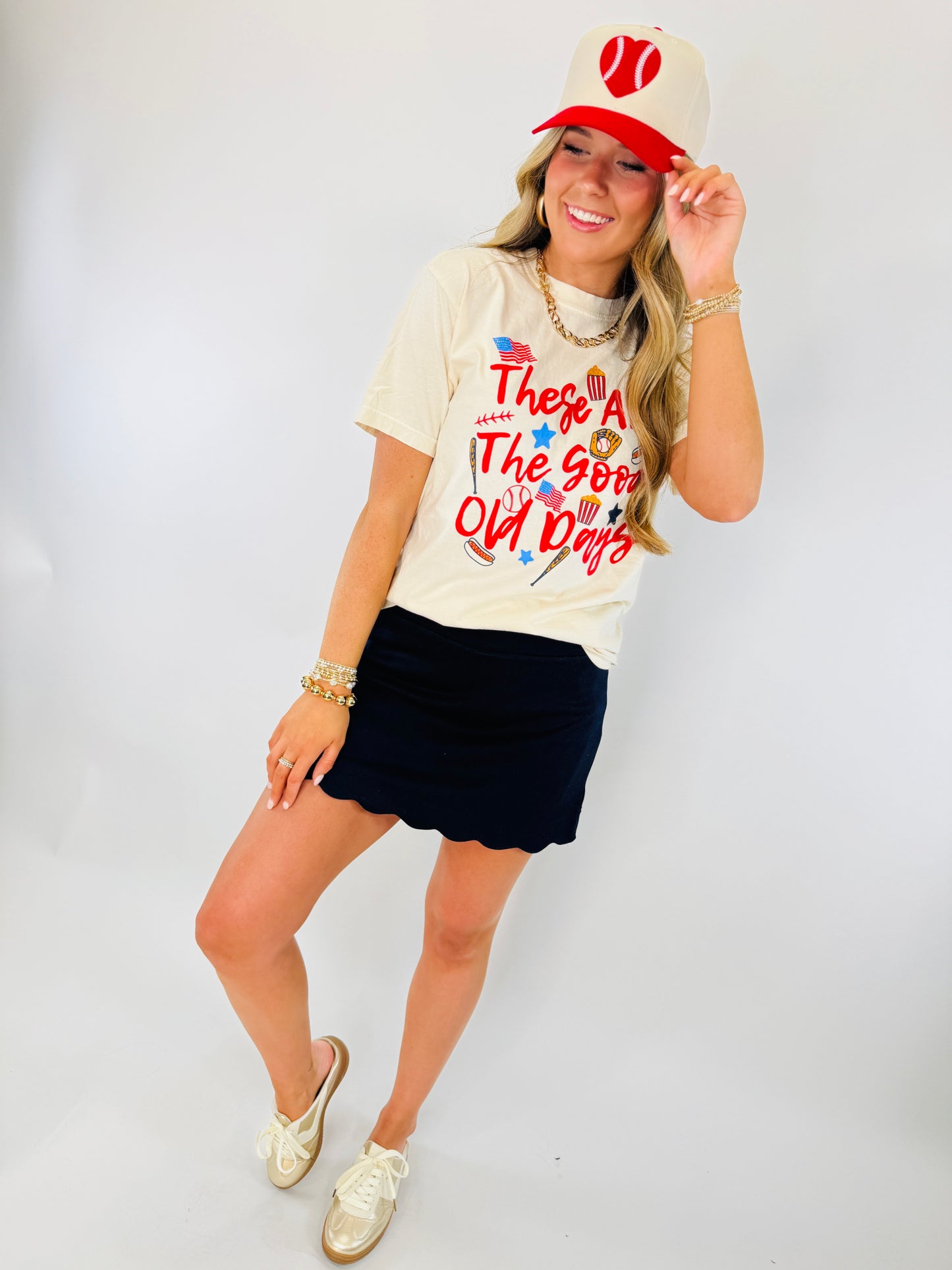 Woman wearing navy blue Kendall Classic Skort with patriotic graphic tee, baseball cap, and gold sneakers.