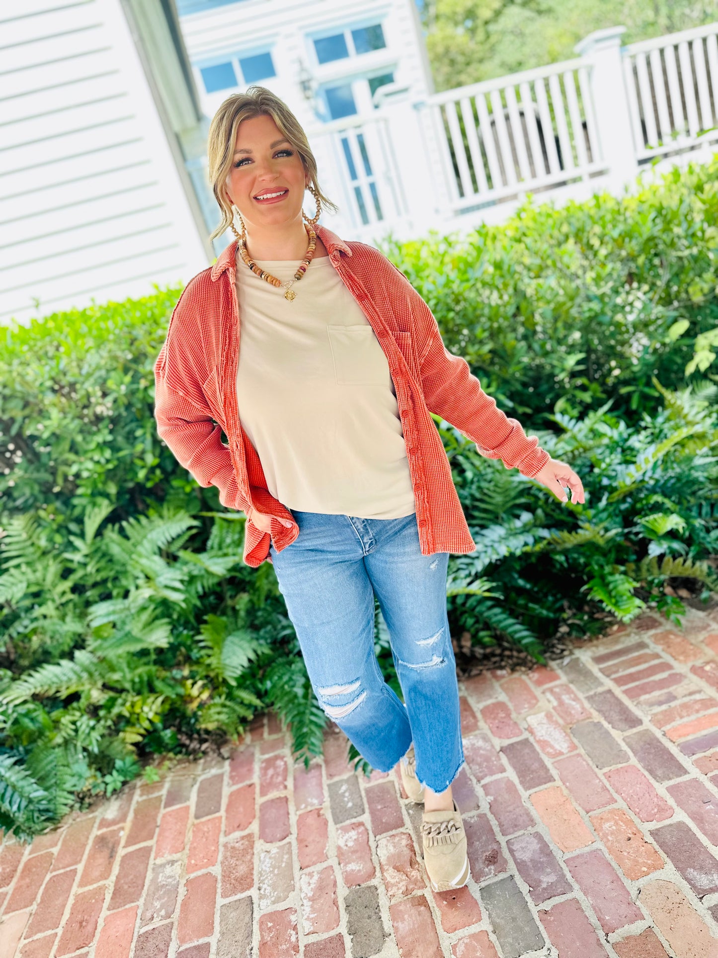Woman wearing cream Tatum top with coral red striped button-up shirt and distressed jeans outdoors