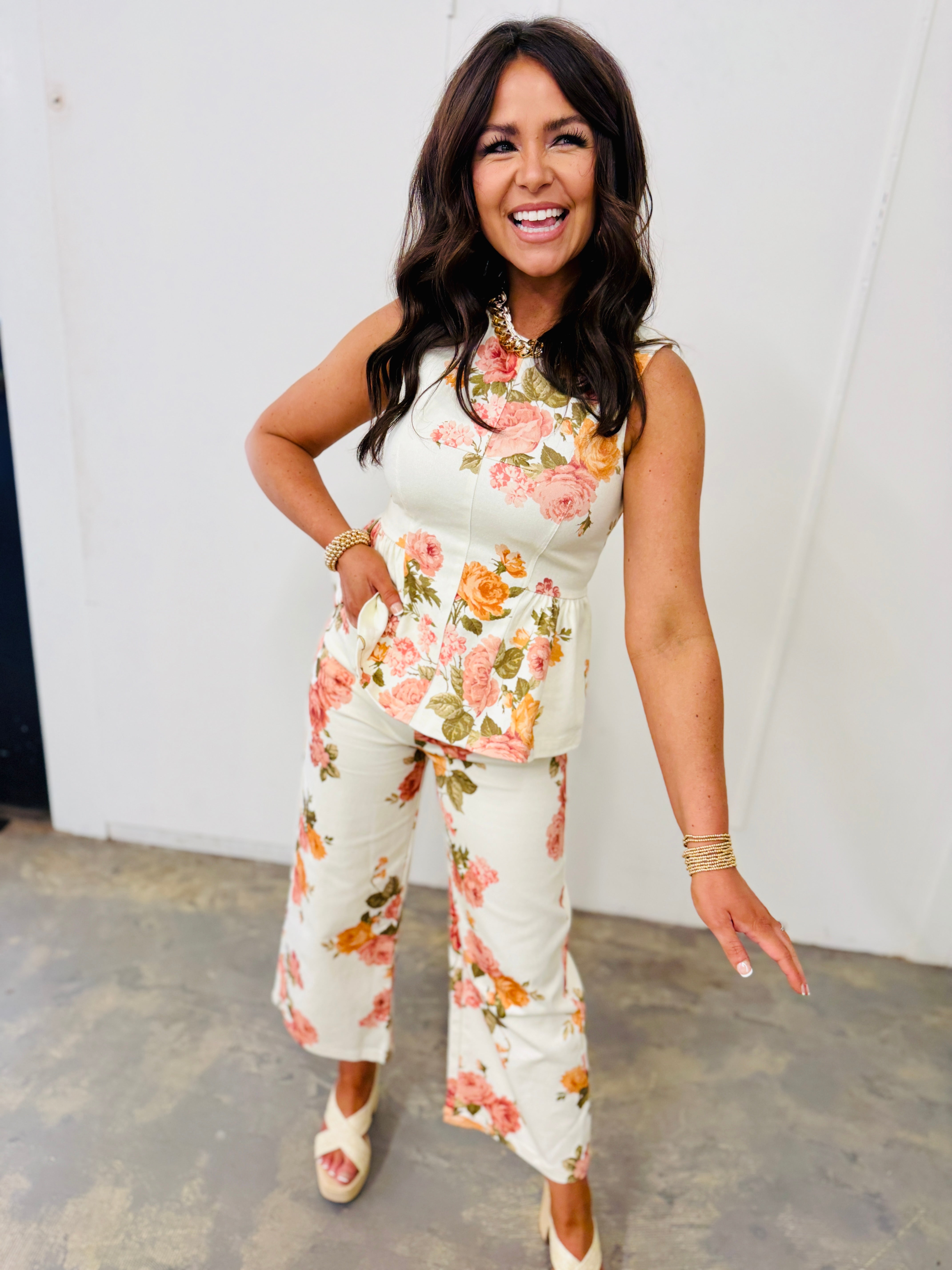 Woman wearing white floral sleeveless top with pink and orange roses, smiling and posing confidently.