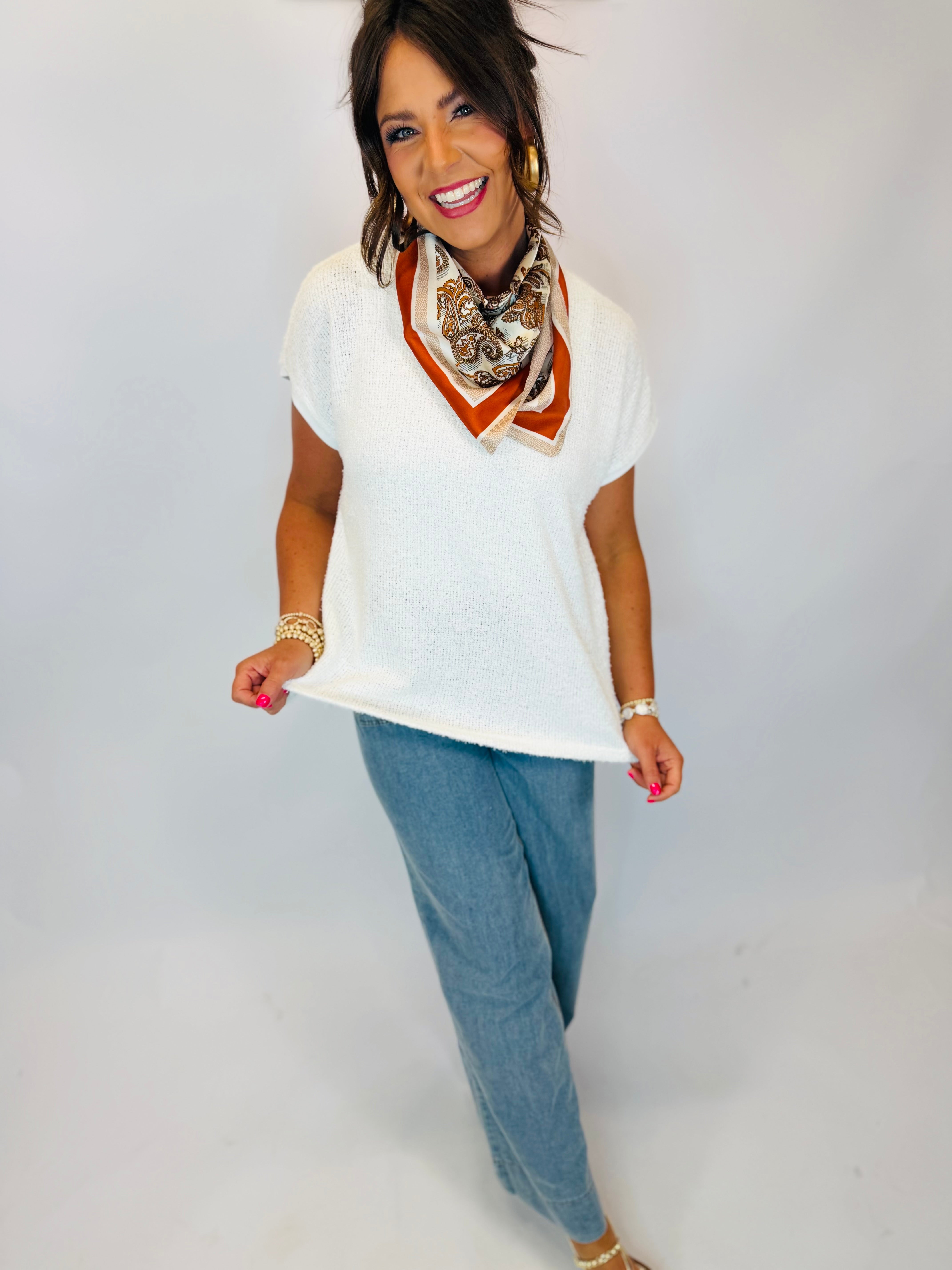 Woman wearing white short-sleeve knit V-neck sweater top with light wash jeans and paisley neck scarf.