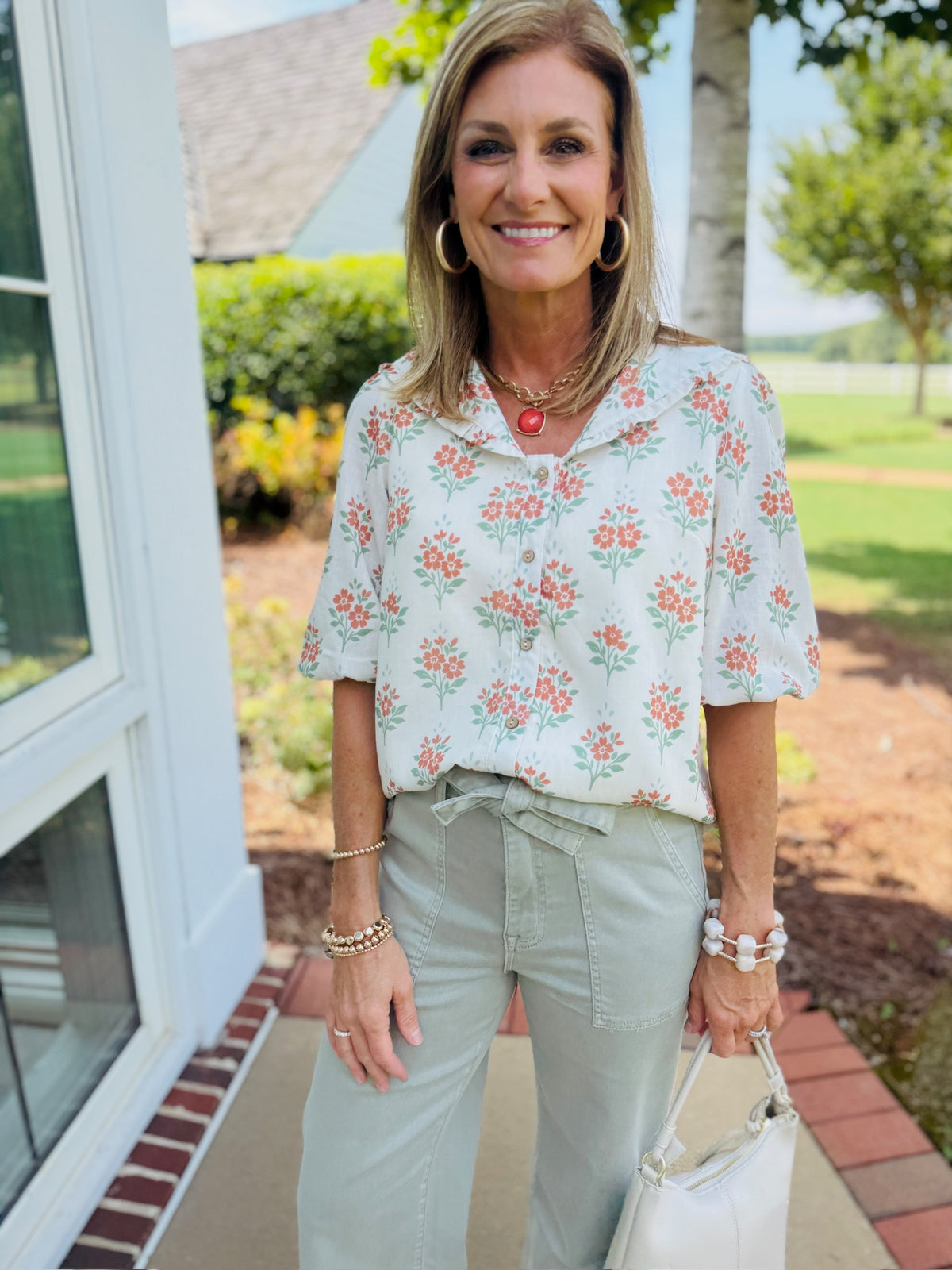 Front view of the Allie cream multi V neck floral top, styled with sage green pants and a cream handbag.
