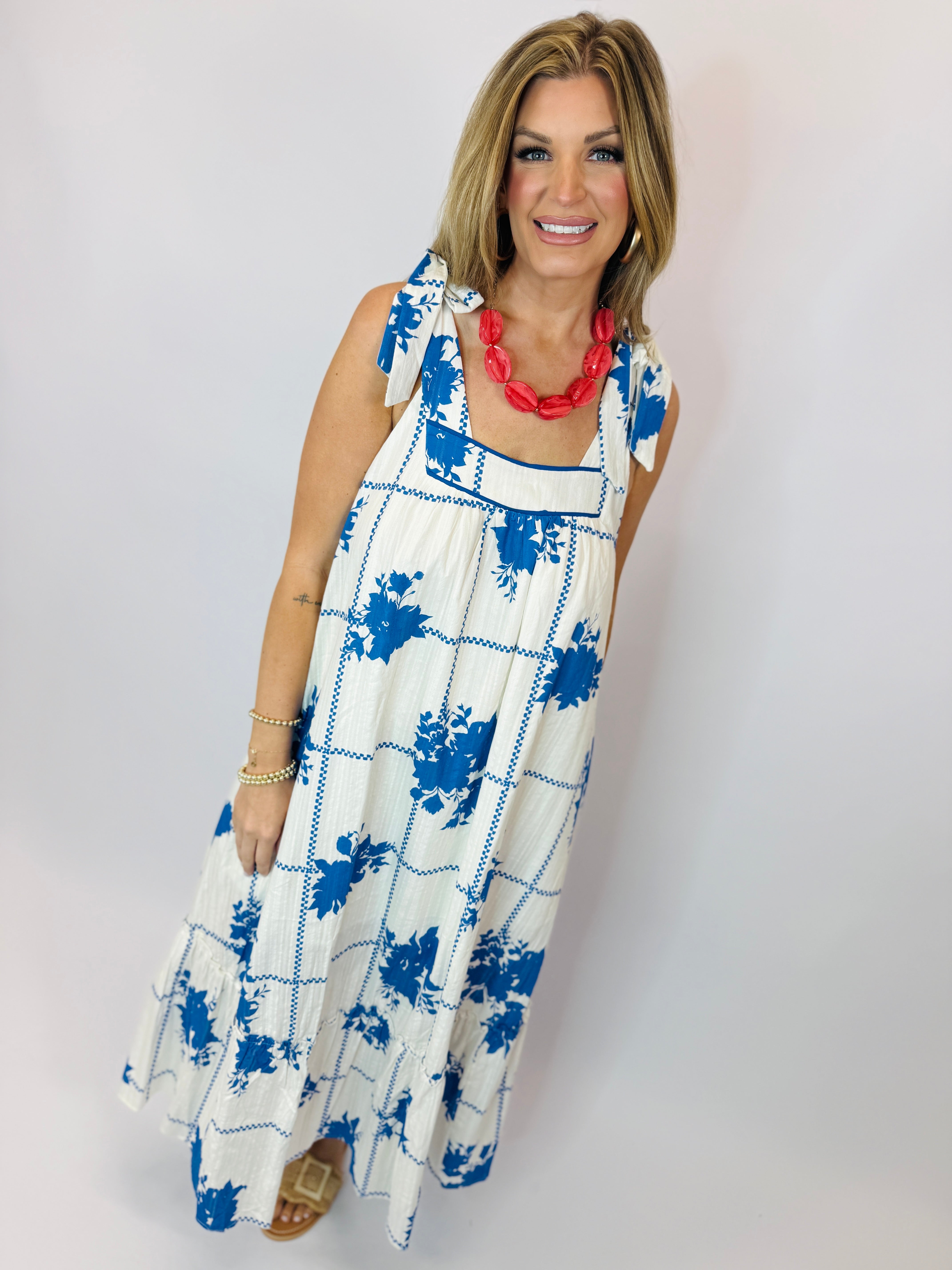 Woman wearing white sleeveless maxi dress with blue floral print and red statement necklace