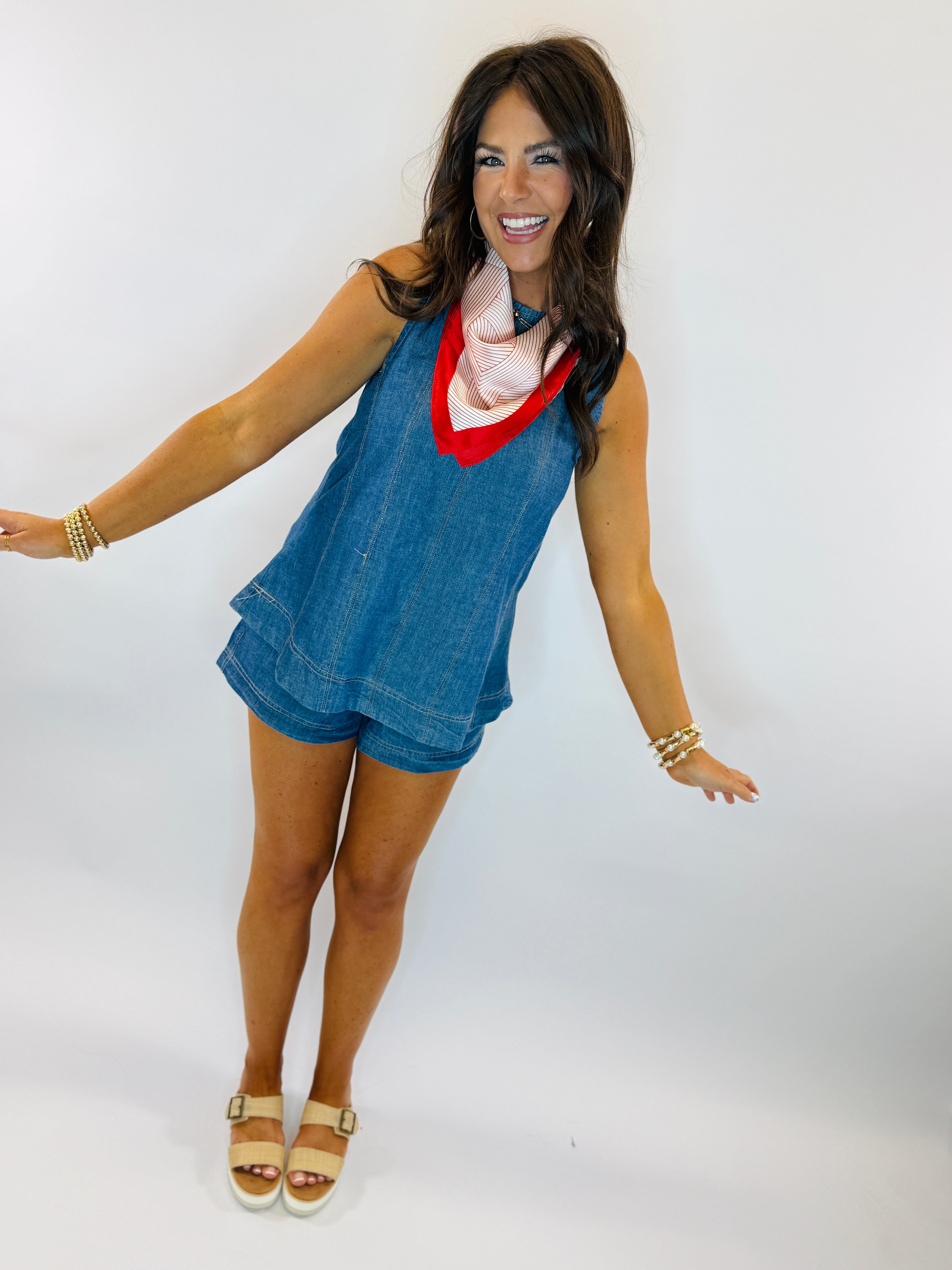 Woman wearing blue denim sleeveless top and shorts set with red and white striped scarf accent.