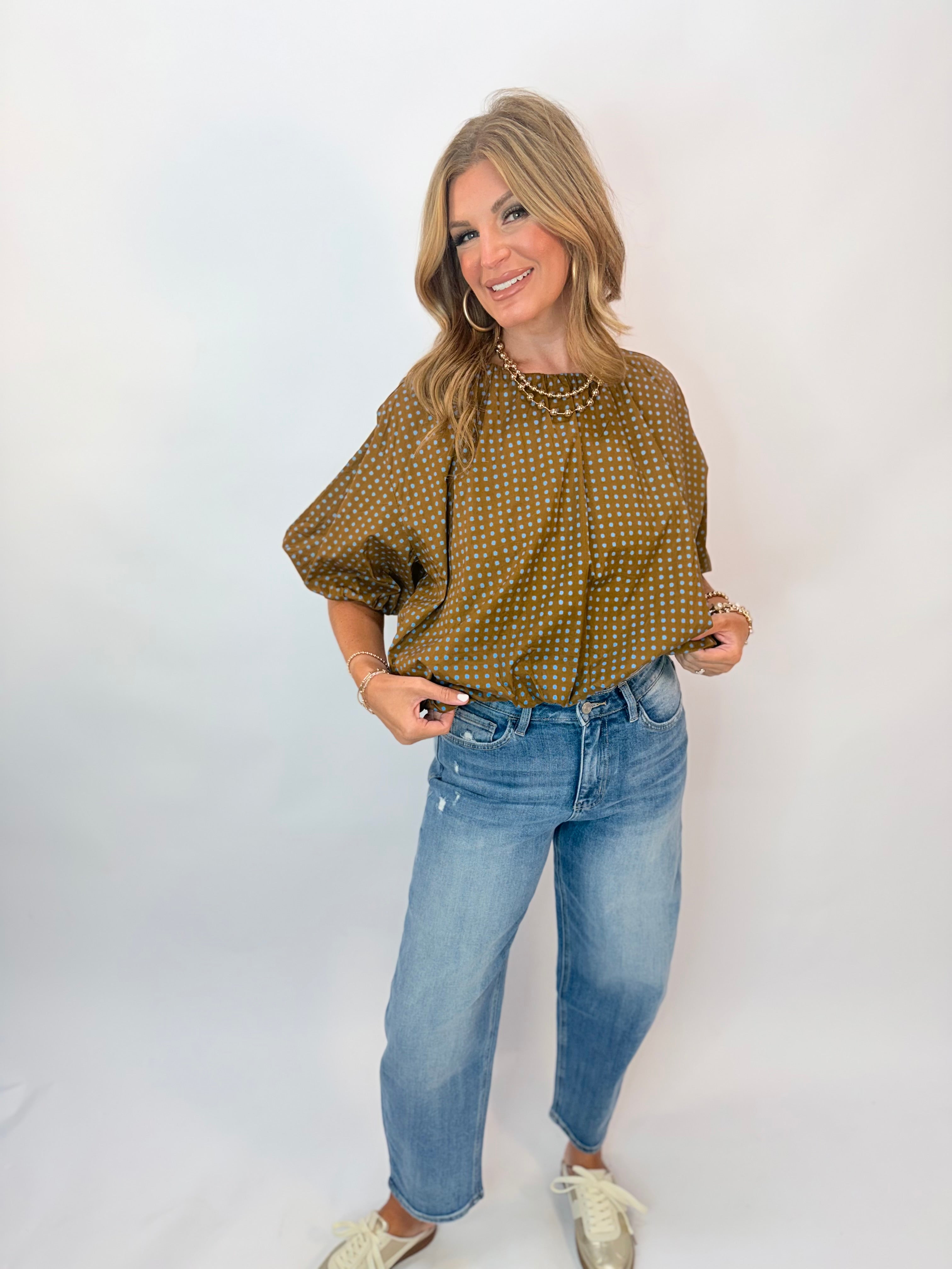 Woman wearing olive green polka dot puff sleeve blouse paired with light wash distressed jeans.