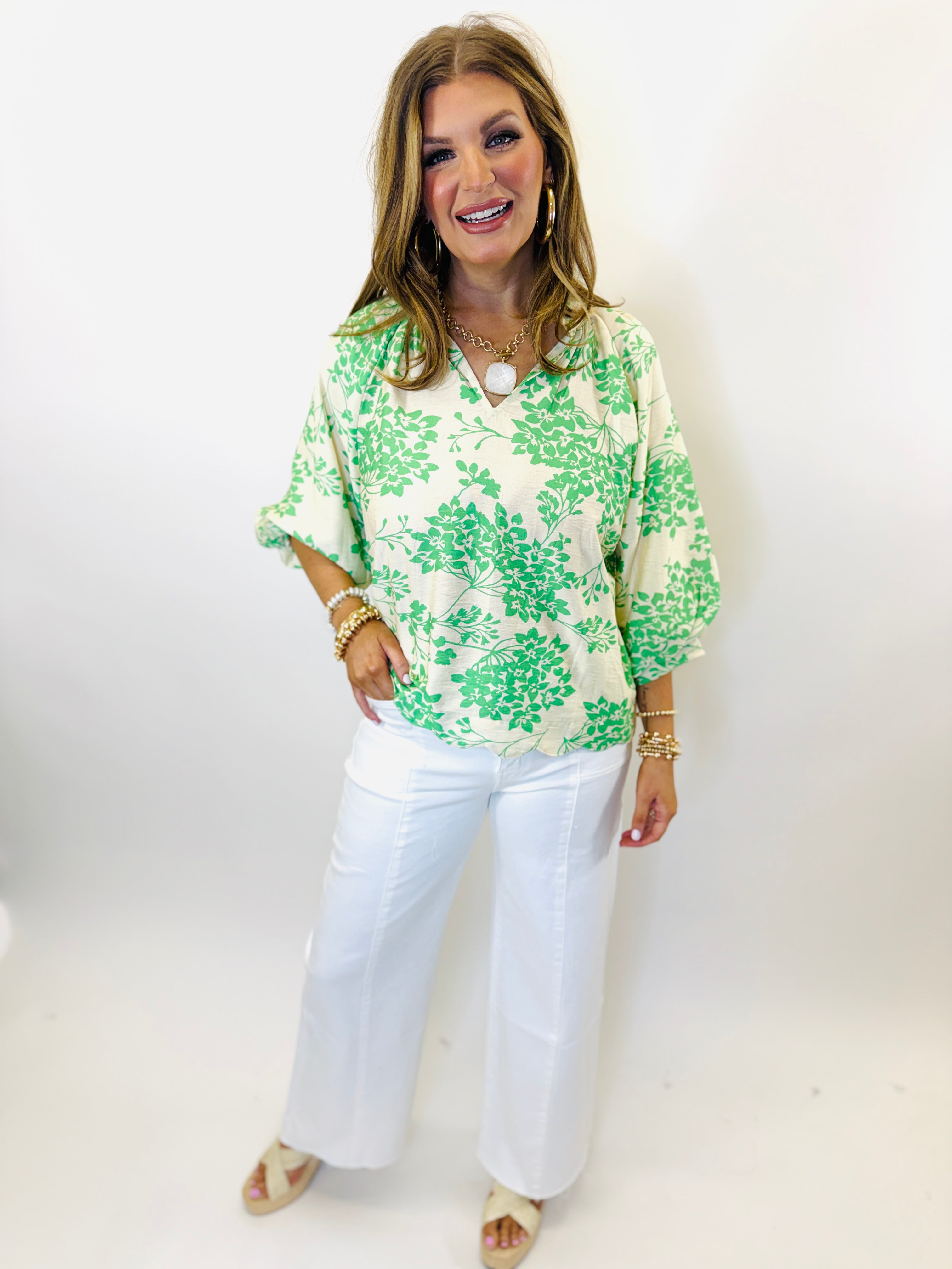 Woman wearing green and white floral print Amelia blouse with three-quarter sleeves and white jeans.