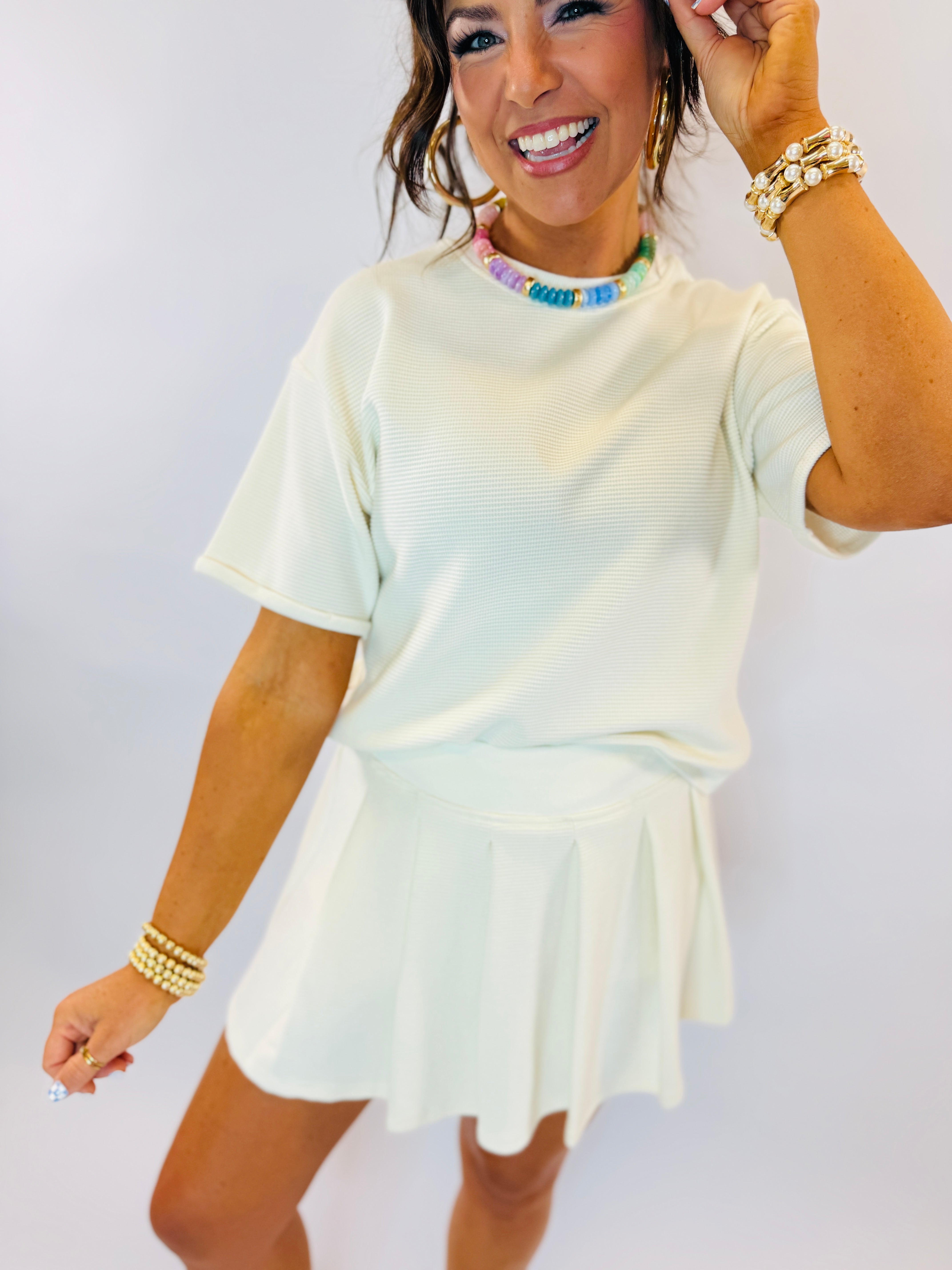 Woman wearing mint green ribbed t-shirt and matching mini skort set with colorful beaded necklace and pearl bracelets.