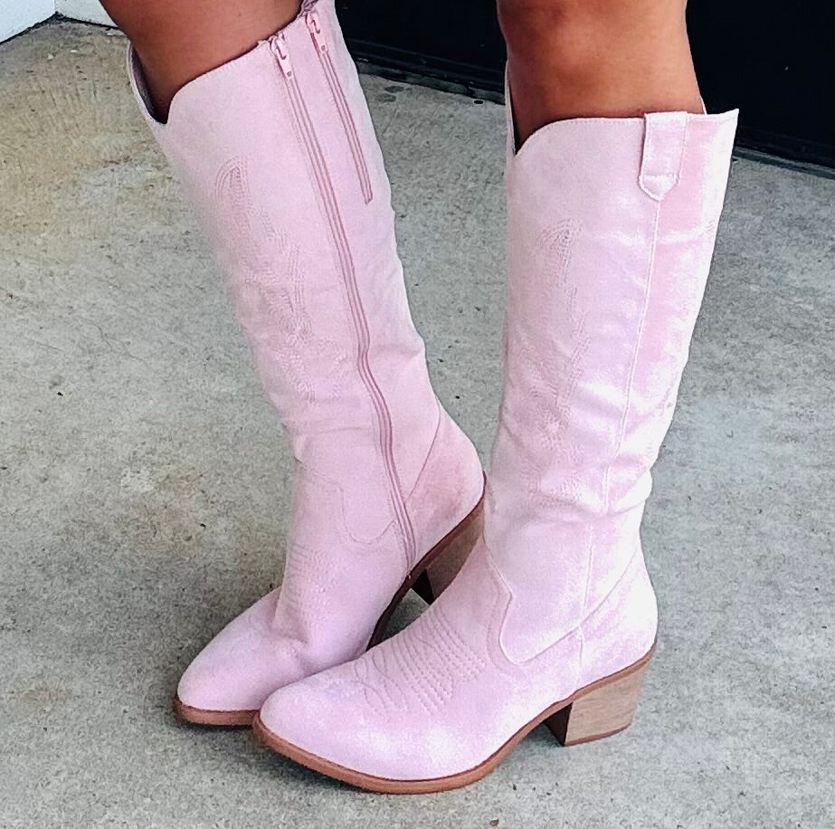 Pink suede tall cowboy boots with embroidered details and block heels worn on concrete surface.