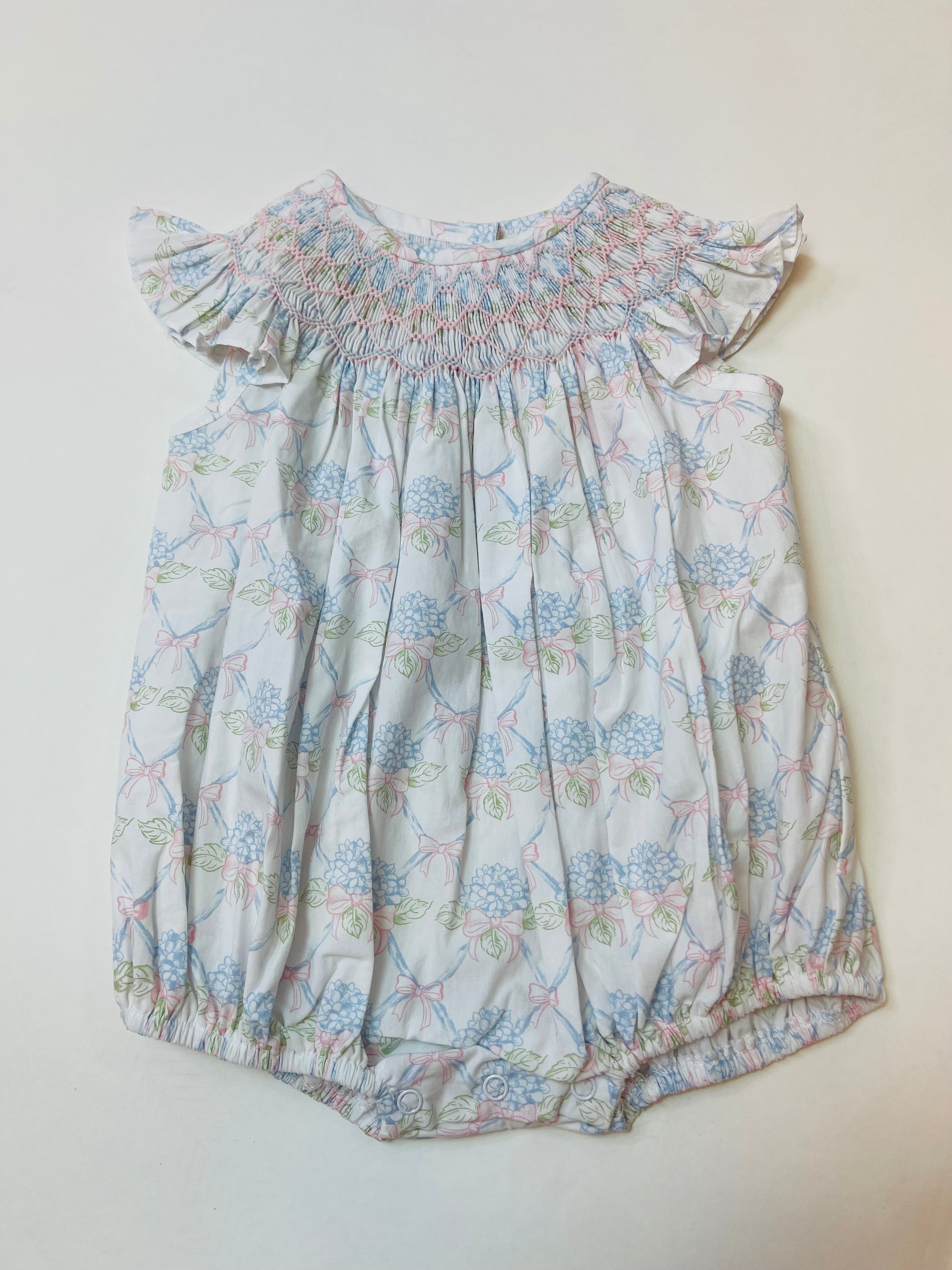 Light blue floral bubble romper with smocked bodice, flutter sleeves, and snap closures at bottom.