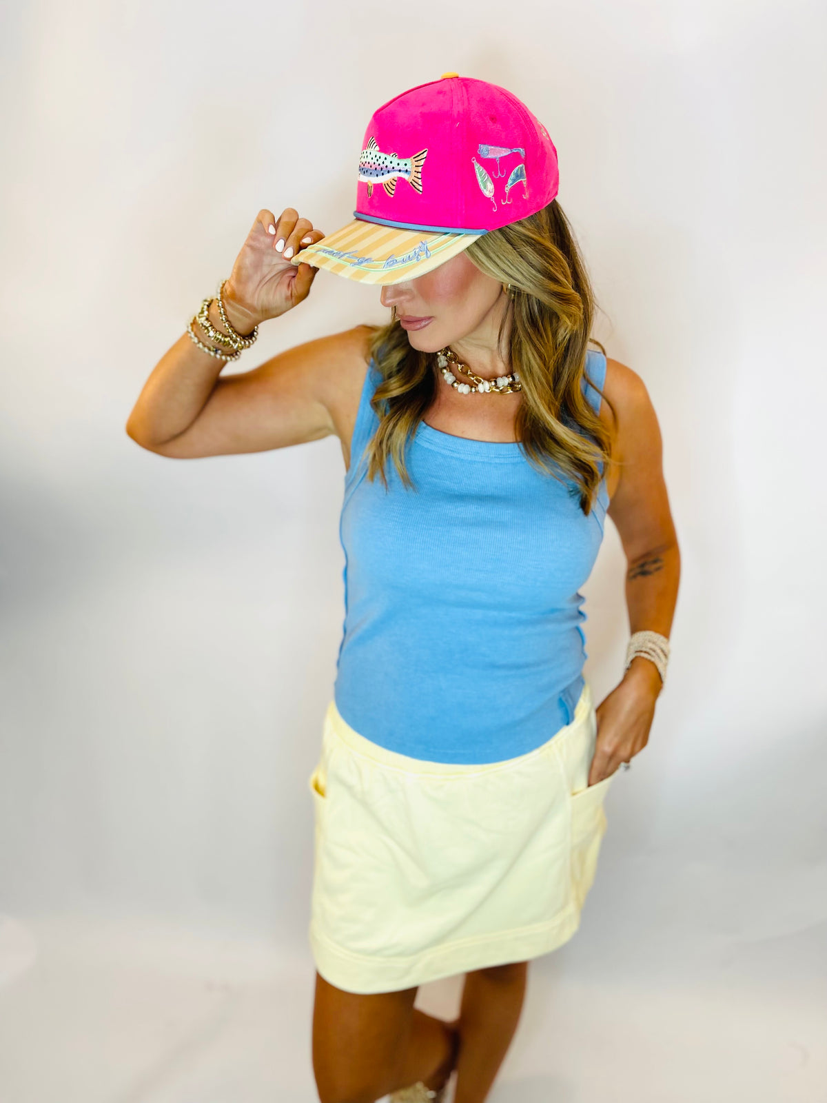 Woman wearing a ribbed light blue sleeveless tank top paired with a yellow mini skirt and pink cap.