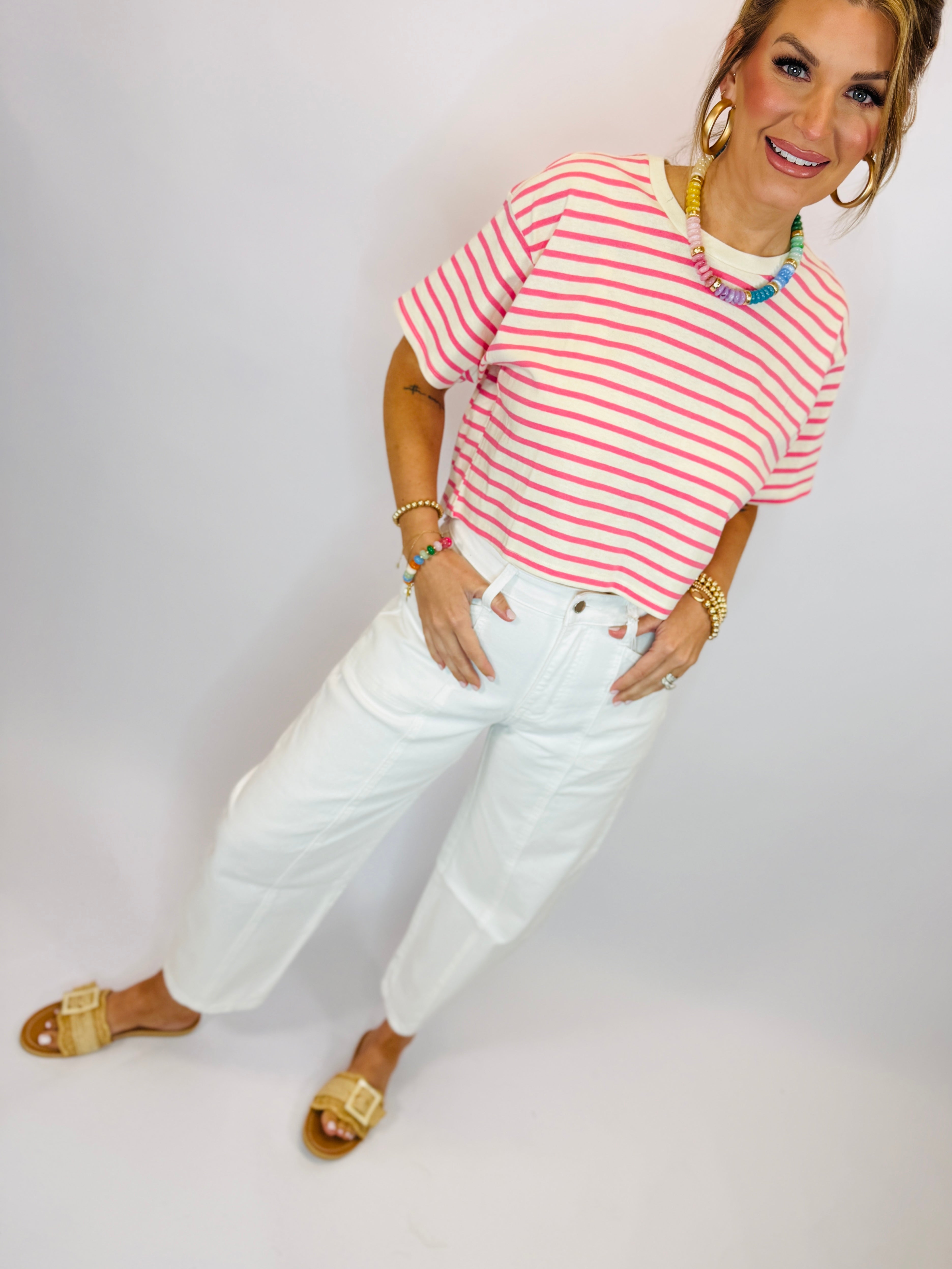 Woman wearing pink and white striped Teagan top with white jeans and gold sandals