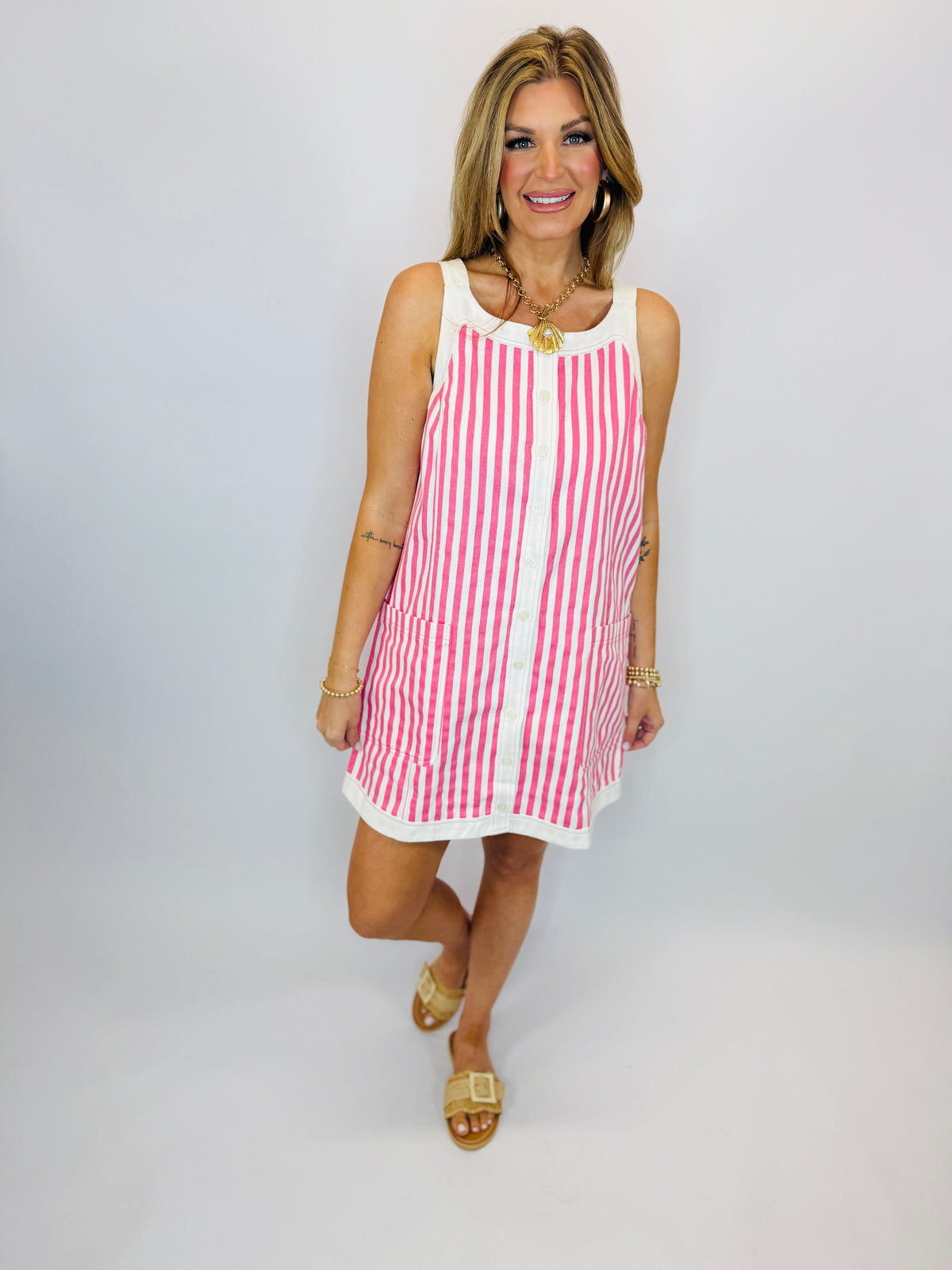 Woman wearing pink and white striped sleeveless mini dress with gold sandals and jewelry