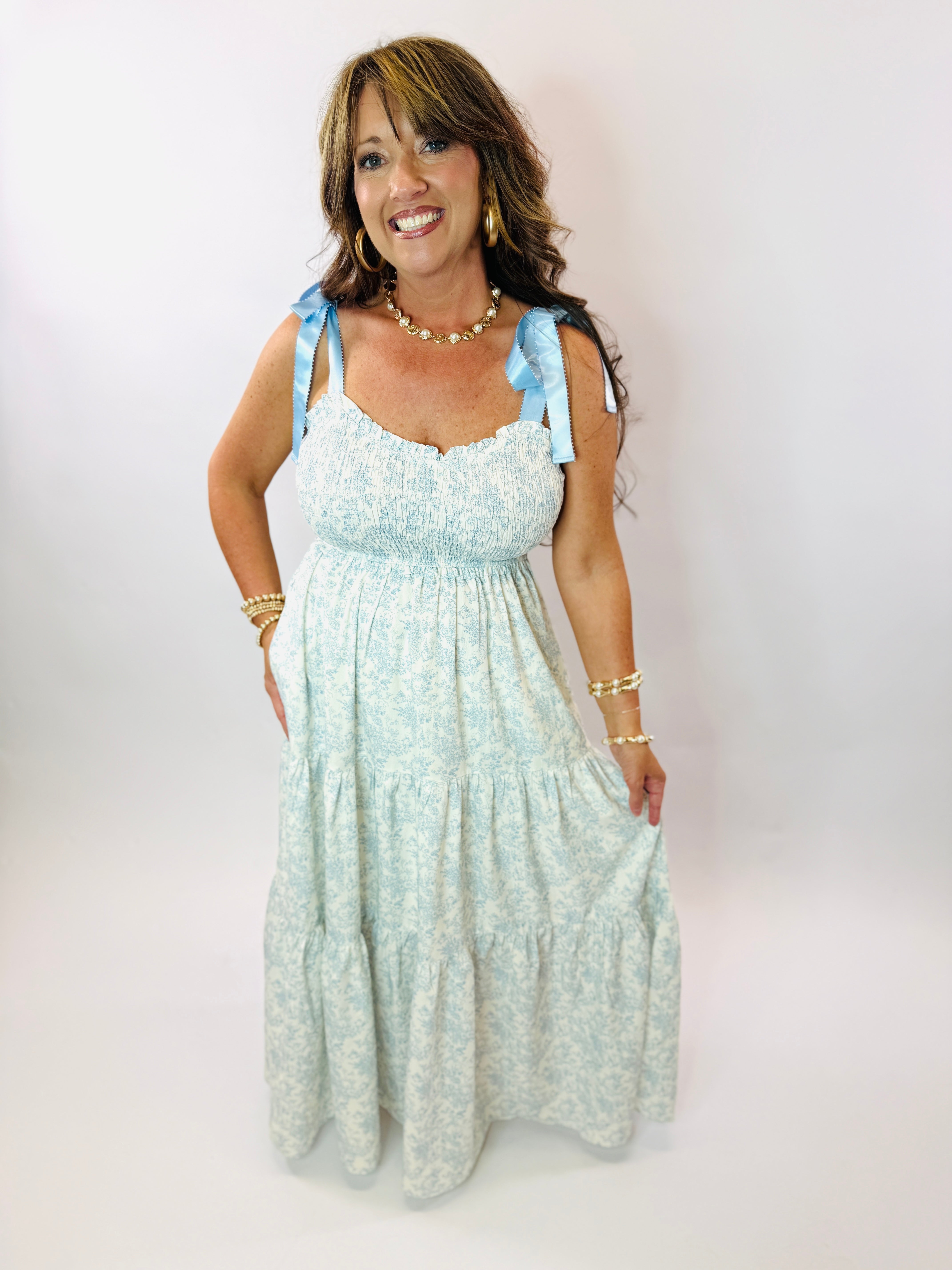Woman wearing light blue floral maxi dress with smocked bodice, tie shoulder straps, and tiered skirt.
