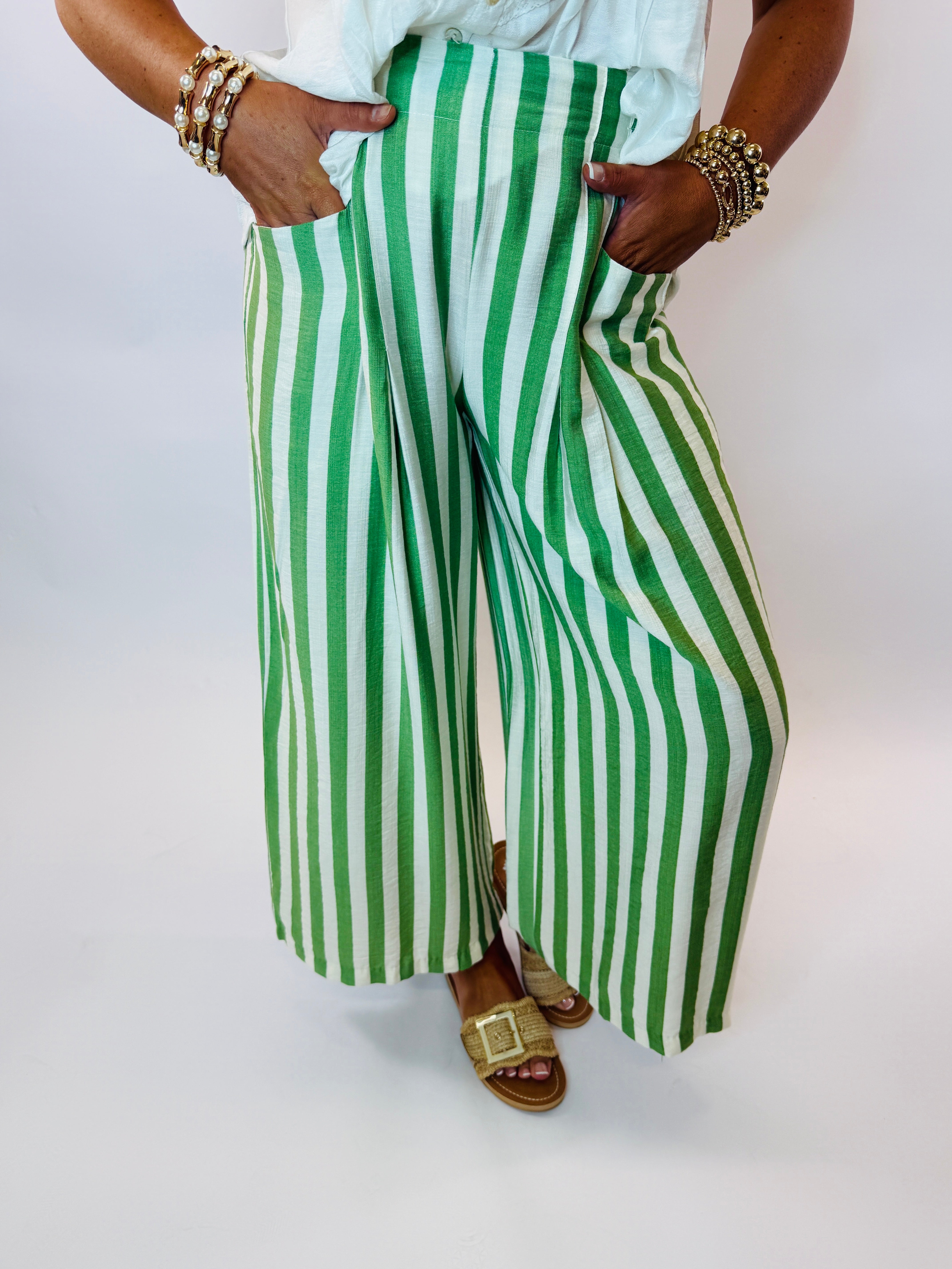 Green and white striped wide-leg pants worn with gold jewelry and sandals against white background.